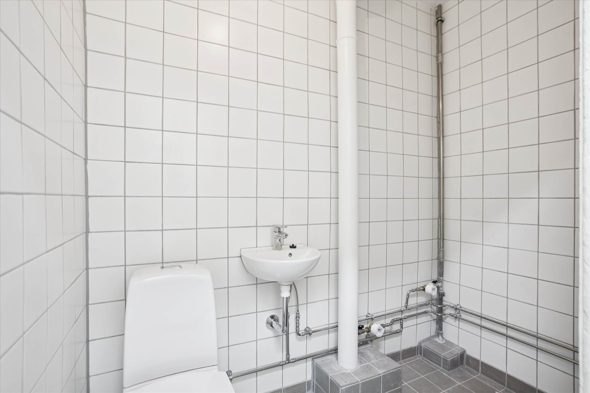 Rent, moderne toilet med hvidt toilet, vask og metalrør monteret på hvide flisede vægge
