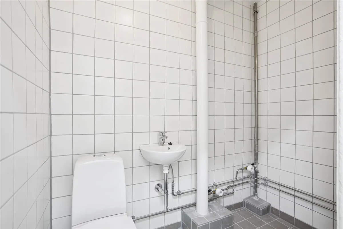 Rent, moderne toilet med hvidt toilet, vask og metalrør monteret på hvide flisede vægge