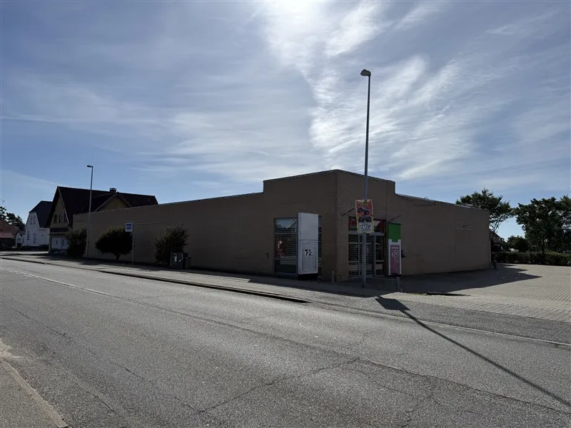 Butikslejemål med stor skygge og plakater på facaden og to lysstofrør foran.