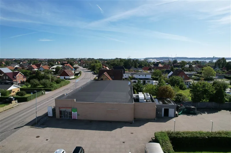 Butikslejemål med parkeringsplads og lager. Lejemålet ligger centralt i Fredericia. På baggrunden ses forskellige huse og
