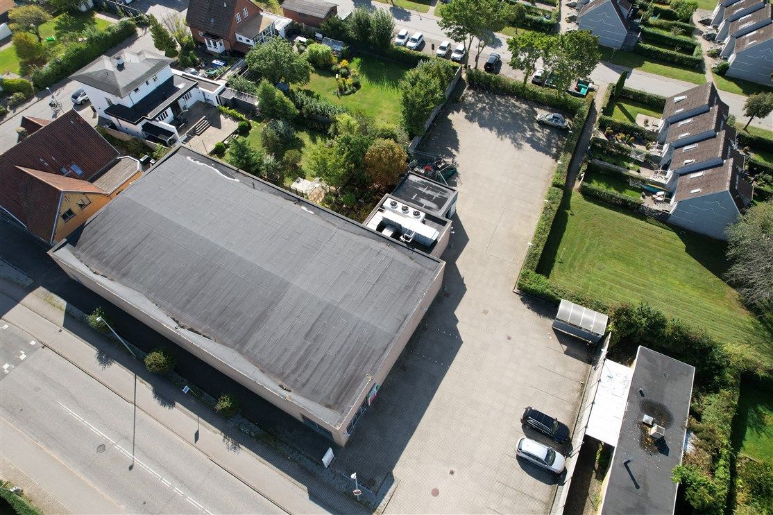 En stor bygning med flere biler parkeret på parkeringspladsen og en grøn eng med træer og buske