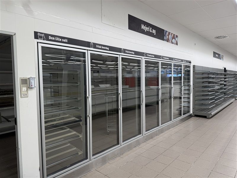 Køligt køleskab i dagligvarebutik med sort tekst "Den lille sult" og "Mejeri & æg" og krydsvise metalhylder og rulleskurve