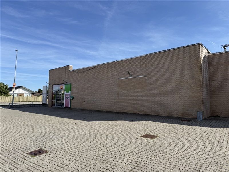 En stor, nyrenoveret bygning med en stor, todelt glasdør og en lysgrå facade. Et større område med brolægning foran bygningen