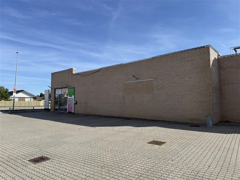 En stor, nyrenoveret bygning med en stor, todelt glasdør og en lysgrå facade. Et større område med brolægning foran bygningen