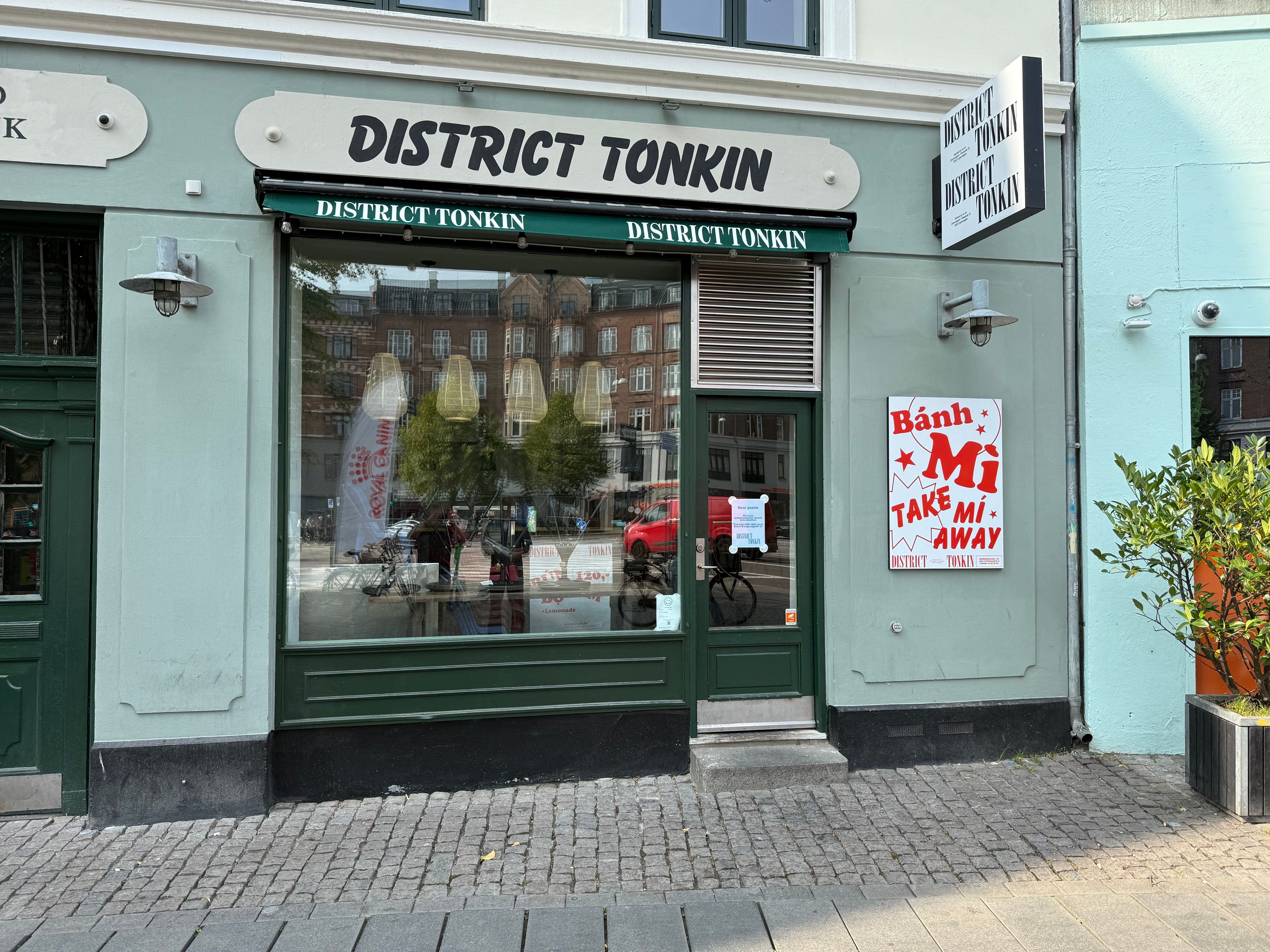 butiksvinduet af District Tonkin på Nørrebrogade 153. Der er en banner med teksten Take Me Away og en plante i en kasse.