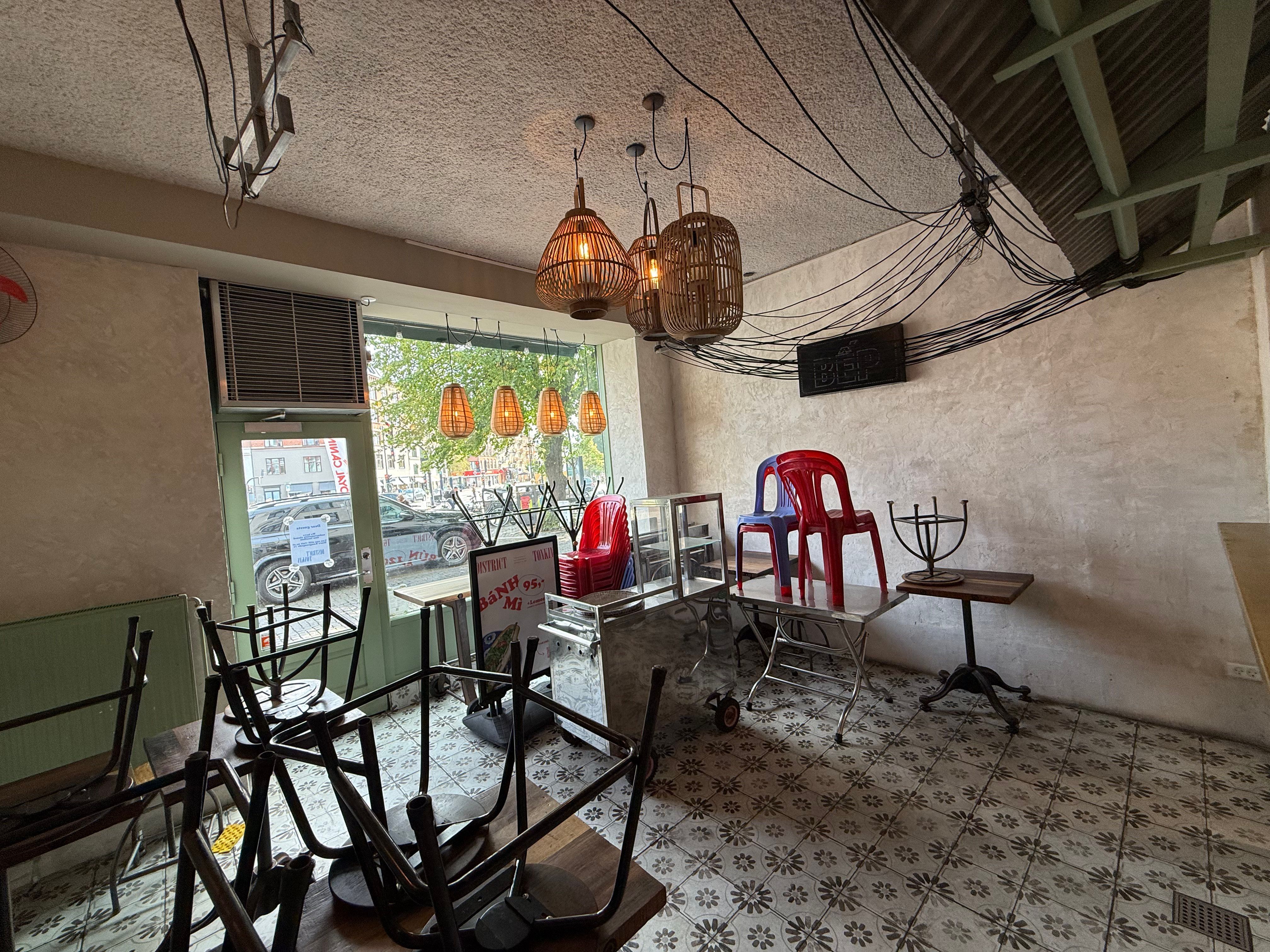 Inde i café med tomme stole og stole stablet i hjørner og udstillingsborde med lysekroner, stole og træborde