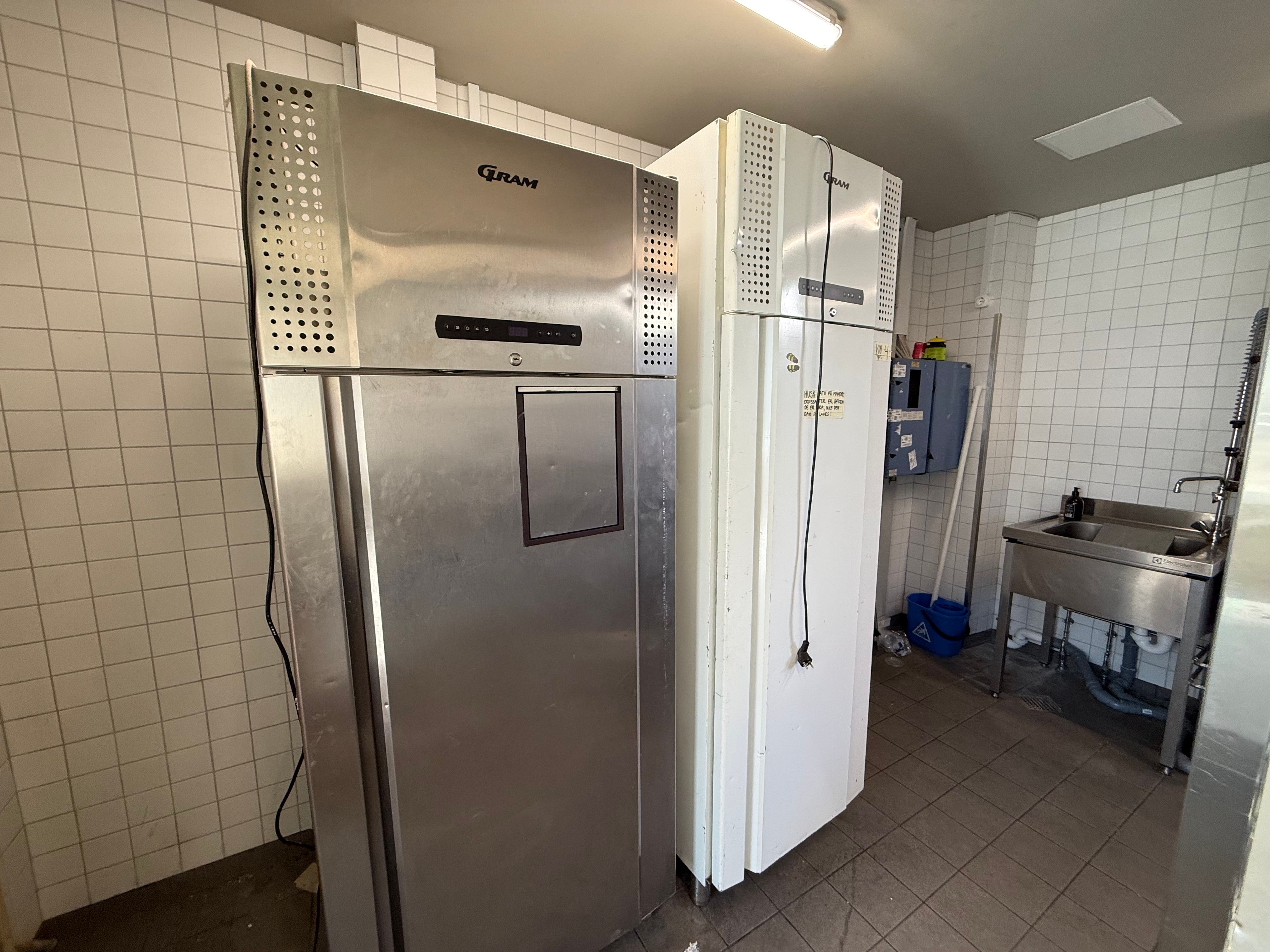 Rummelig køkkenrum med dobbelt køleapparat, skraldspande og renseriudstyr. Forretning med køkkenfaciliteter i centrum af København.