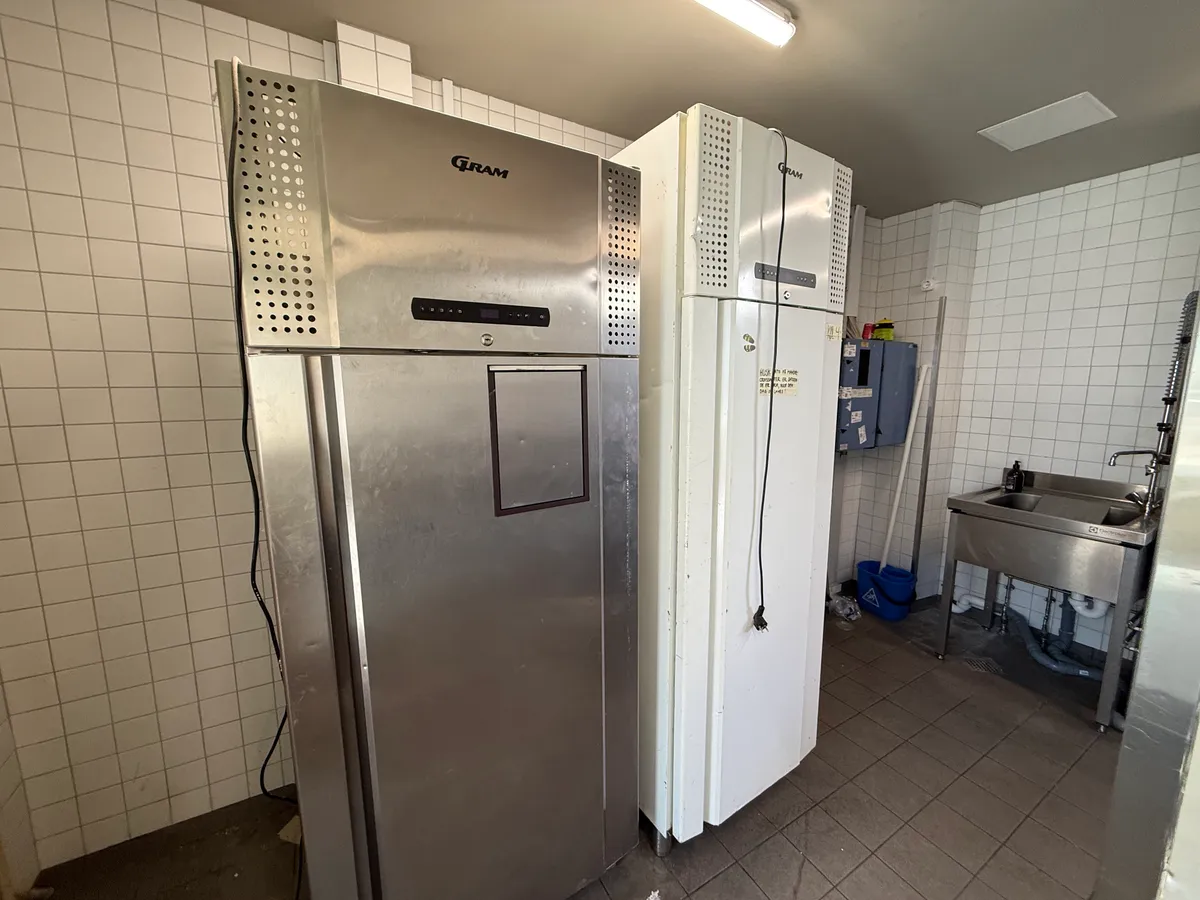 Rummelig køkkenrum med dobbelt køleapparat, skraldspande og renseriudstyr. Forretning med køkkenfaciliteter i centrum af København.