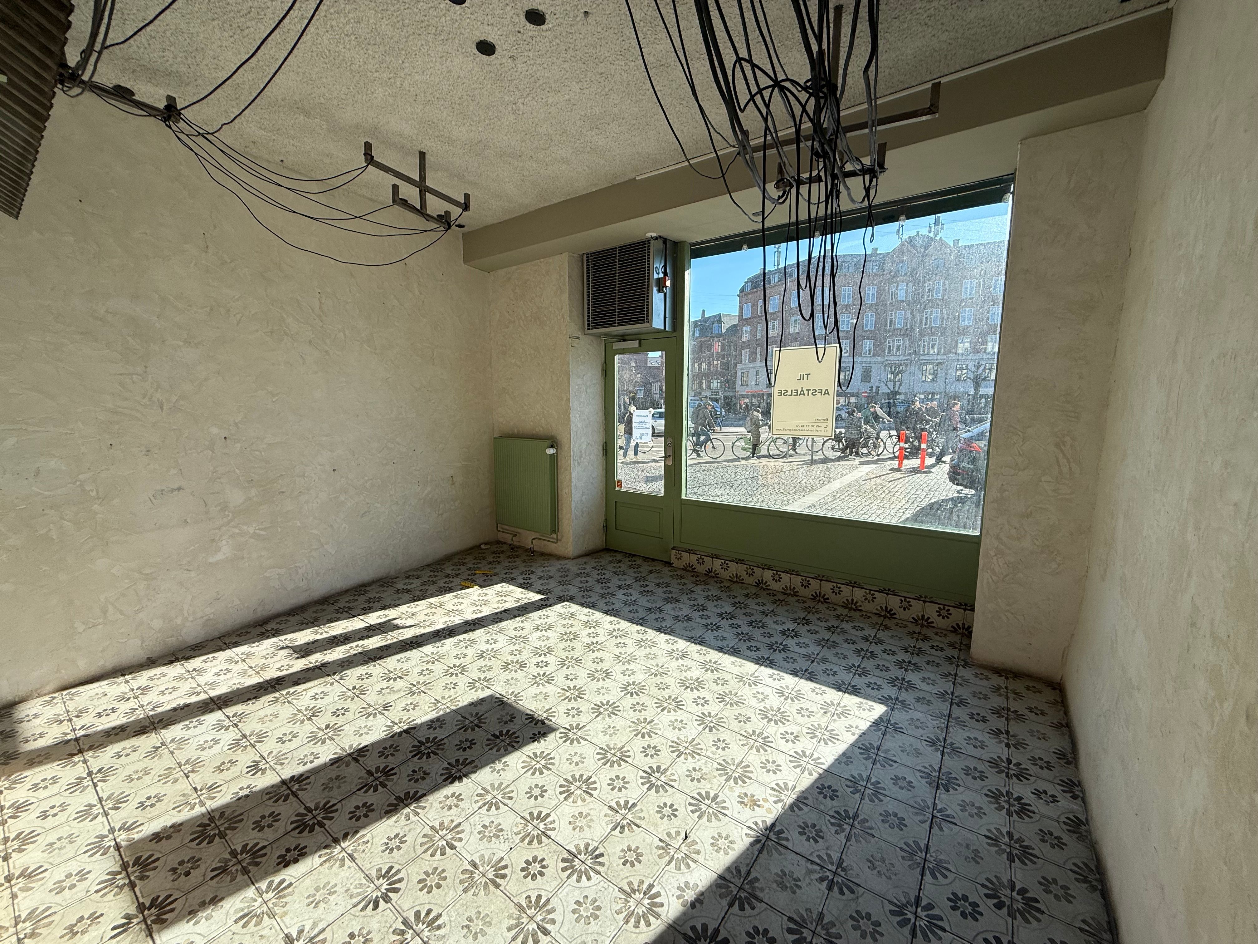 Take-away butik på Nørrebrogade med større vinduer og luftkanal til køling. Grønne døre og terrasse uden for og brostensbelagt vej udenfor.