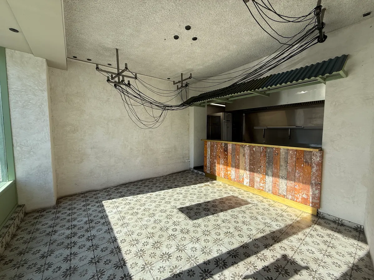 Et ubenyttet rum med køkken og vinduer til leje på Nørrebrogade 153, København N, med tømmervæg og solstråler.