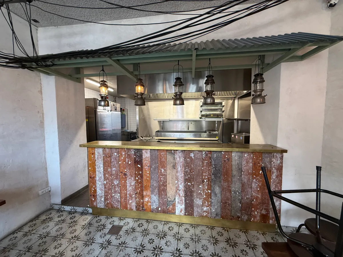 Køkken med rustfrit stålapparater, rustne træbrædder og lysekroner i loftet. Et moderne og industrielt design med en lysegul