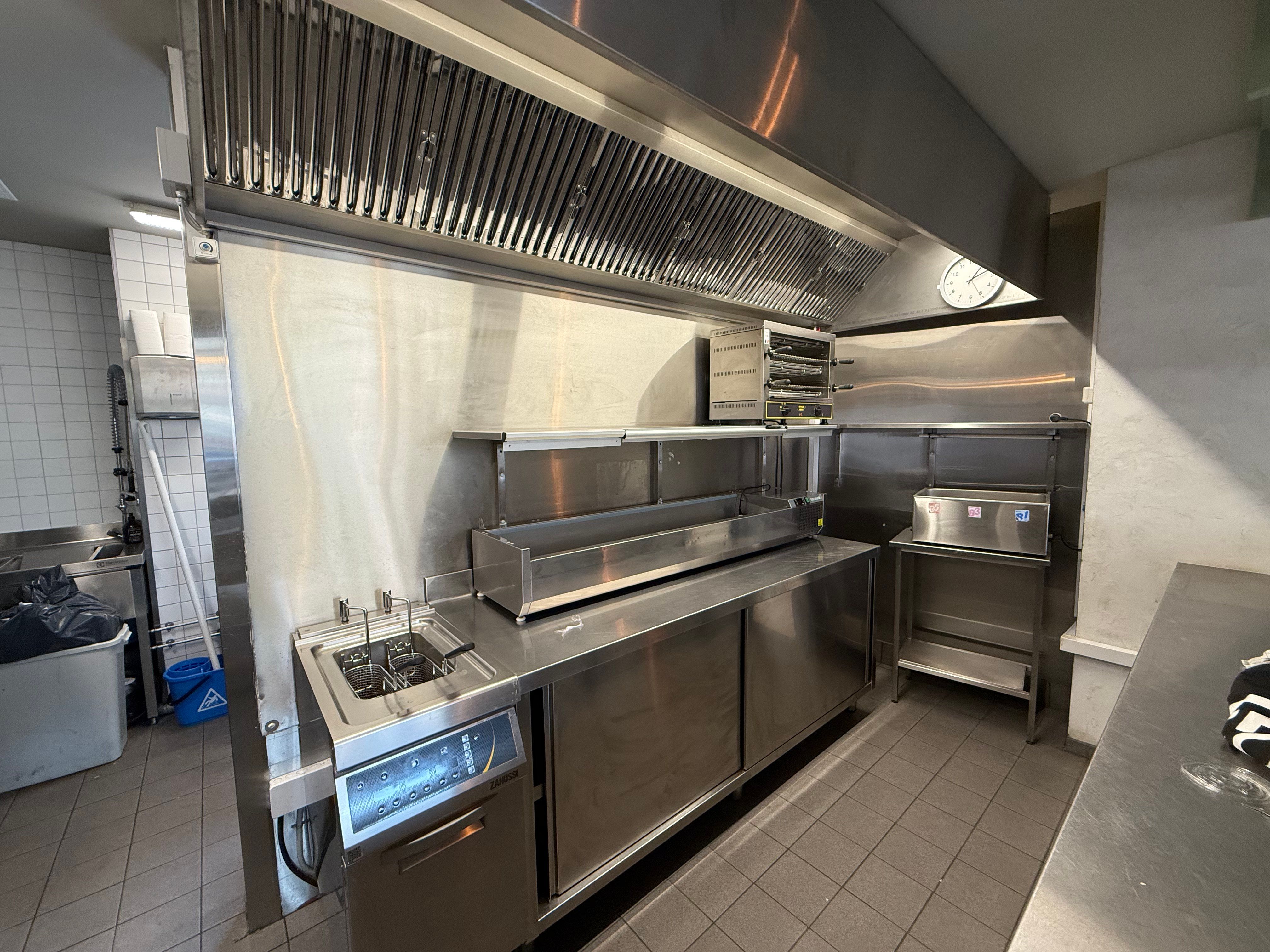 Professionelt køkken med moderne apparater, rensningsudstyr og en stor ventileringsluge på loftet