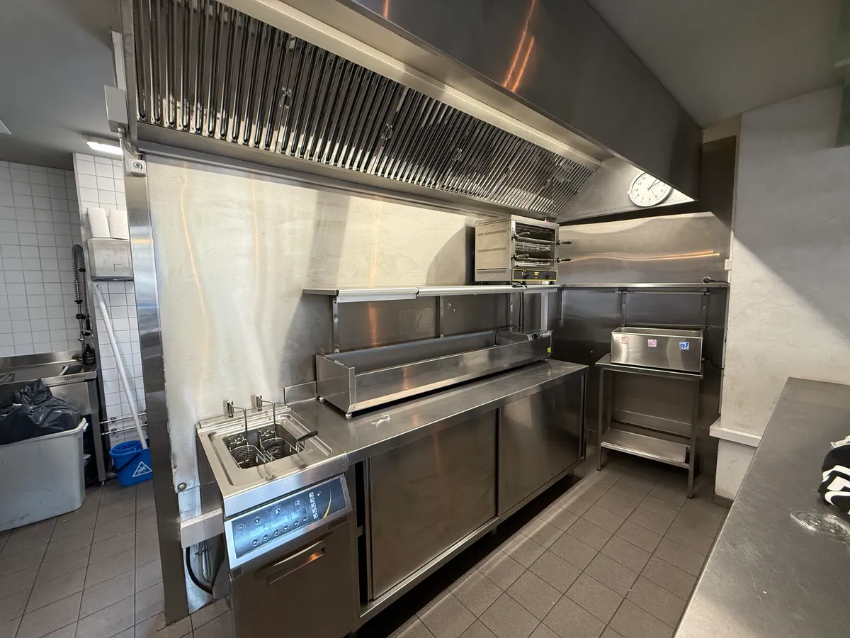 Professionelt køkken med moderne apparater, rensningsudstyr og en stor ventileringsluge på loftet