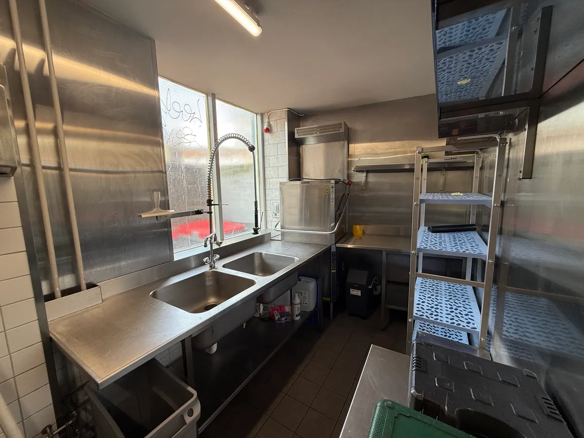 I et kommercielt køkken er der dobbeltvask og flere metalreoler samt en stående ovn og et køleskab.
