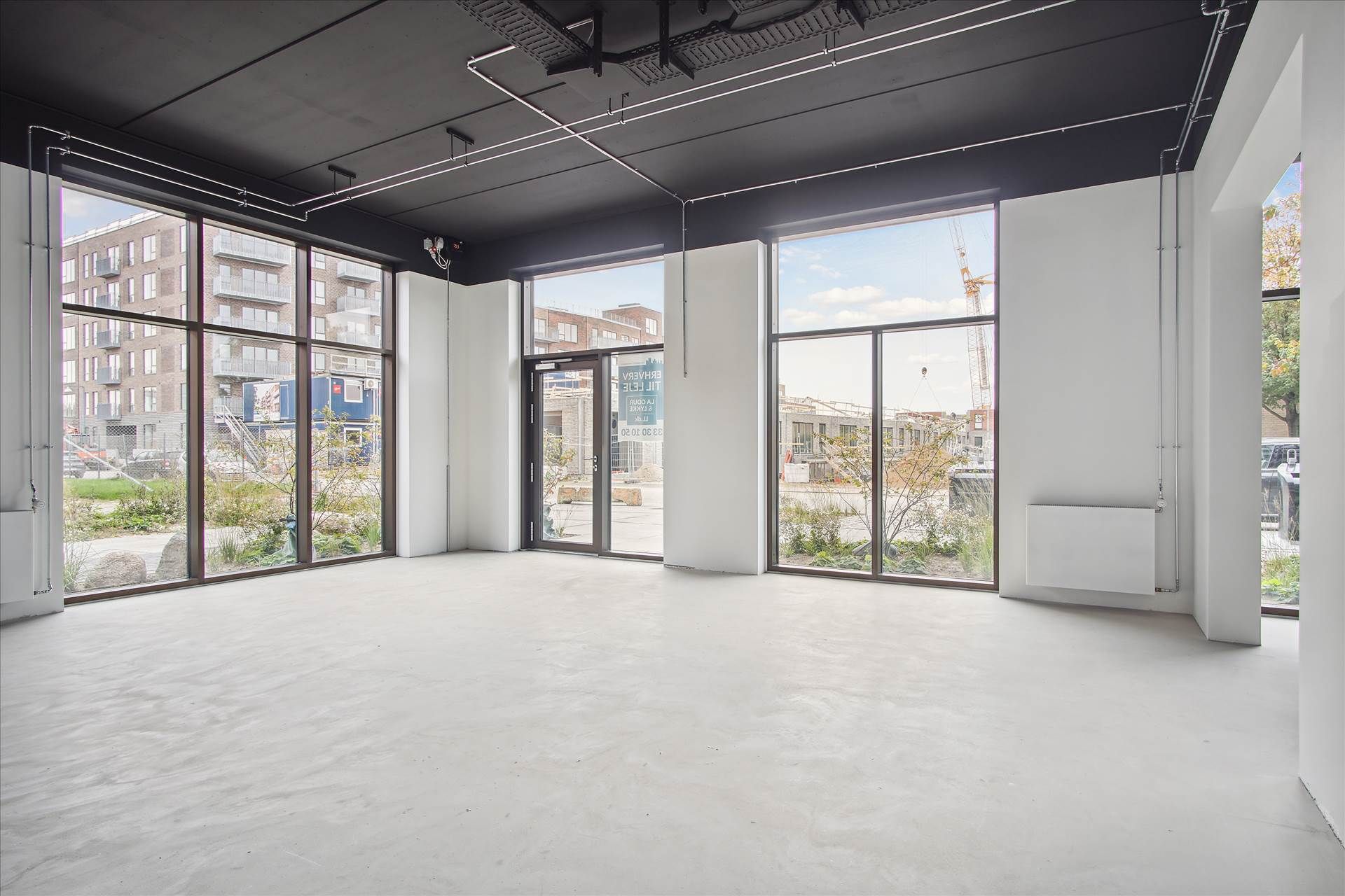 En tom, hvid, moderne og minimalistisk interiør med store vinduer og glasdøre samt en åben dør og et vindue på vej