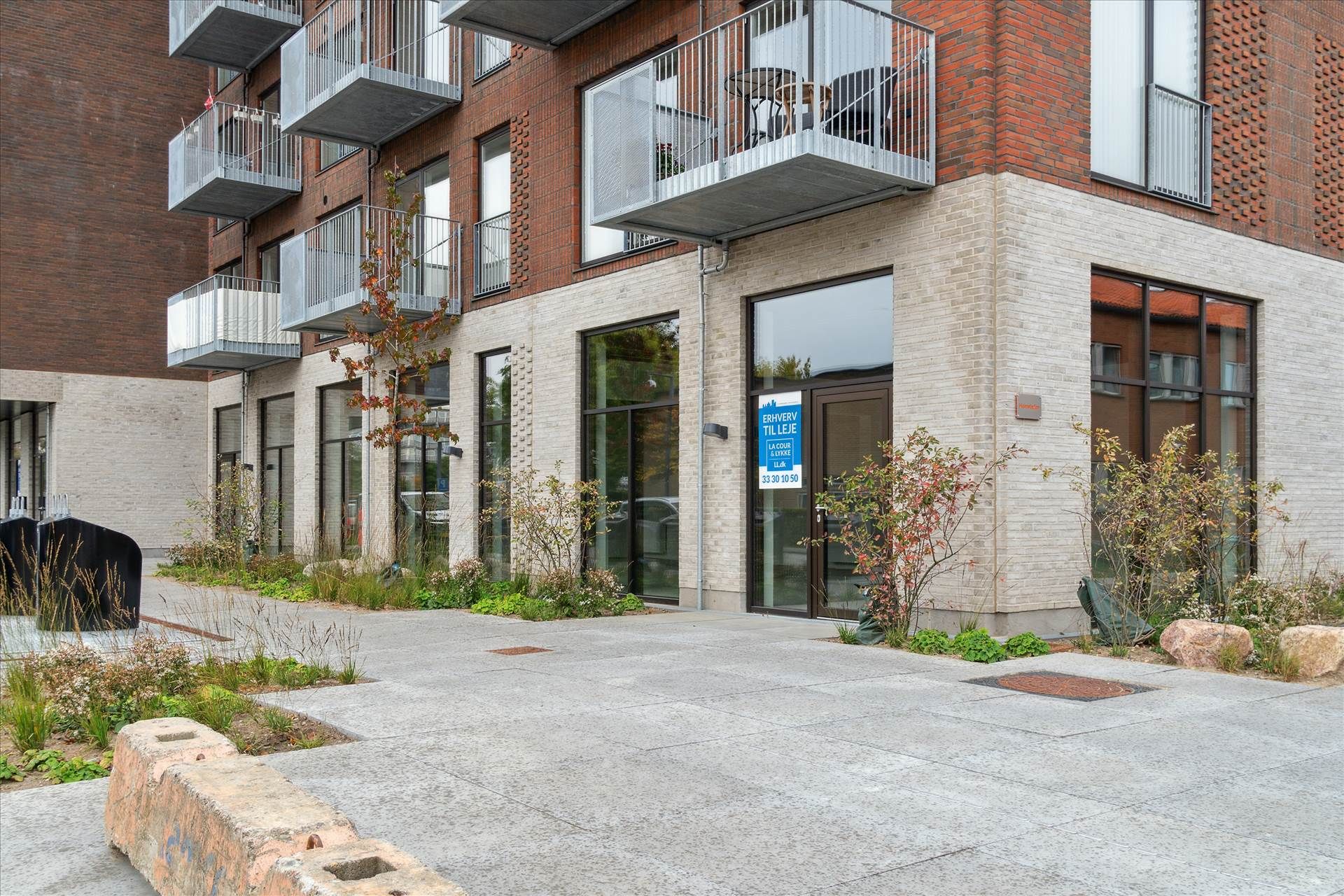 Et moderne lejlighedskompleks med terrasser og glasvinduer, hvor en lejlighed ud lejes til 33,30 kr. pr. m2