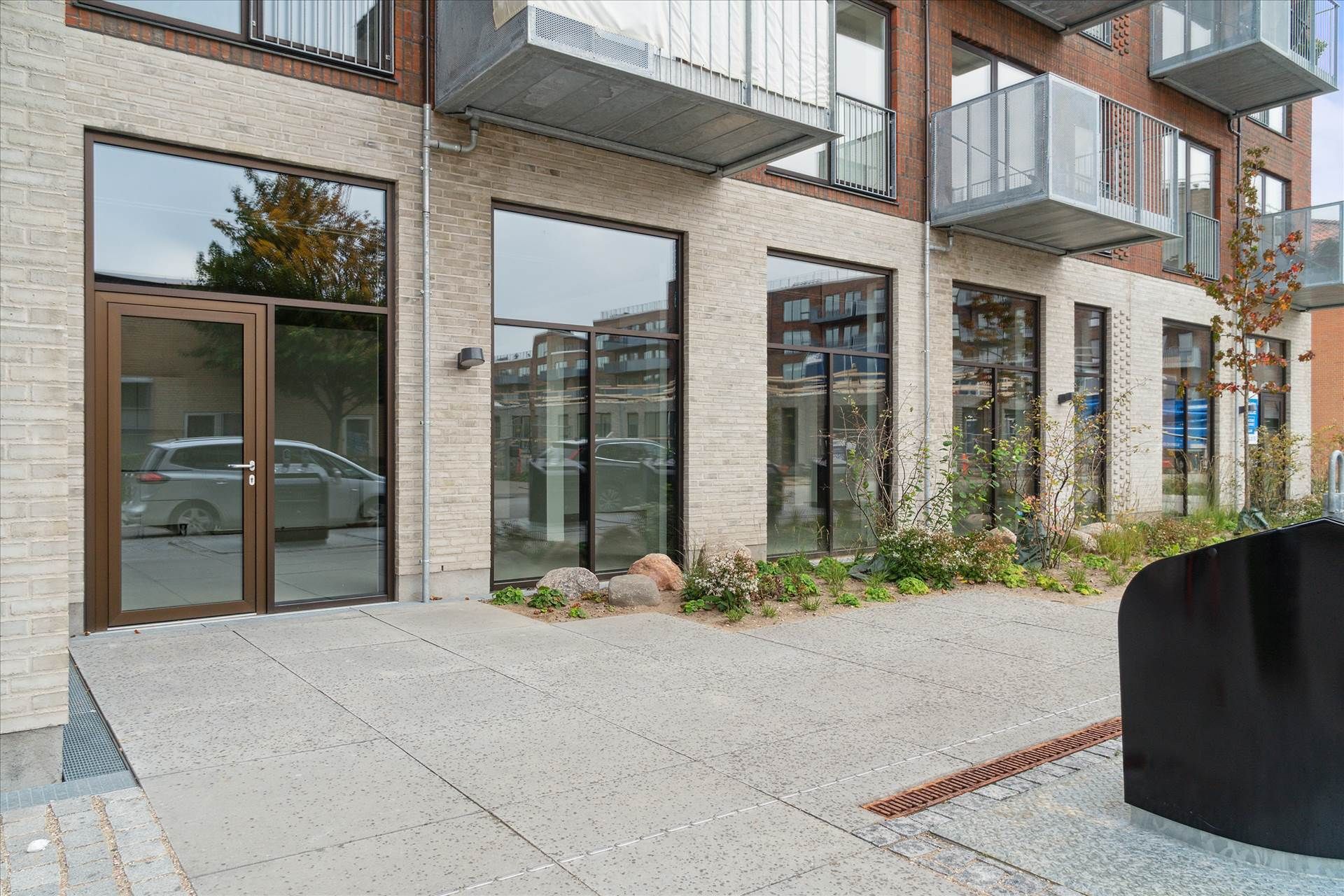 Bygning med glasdøre og store ruder, flere balkoner og terrasser, samt en statue og planter foran