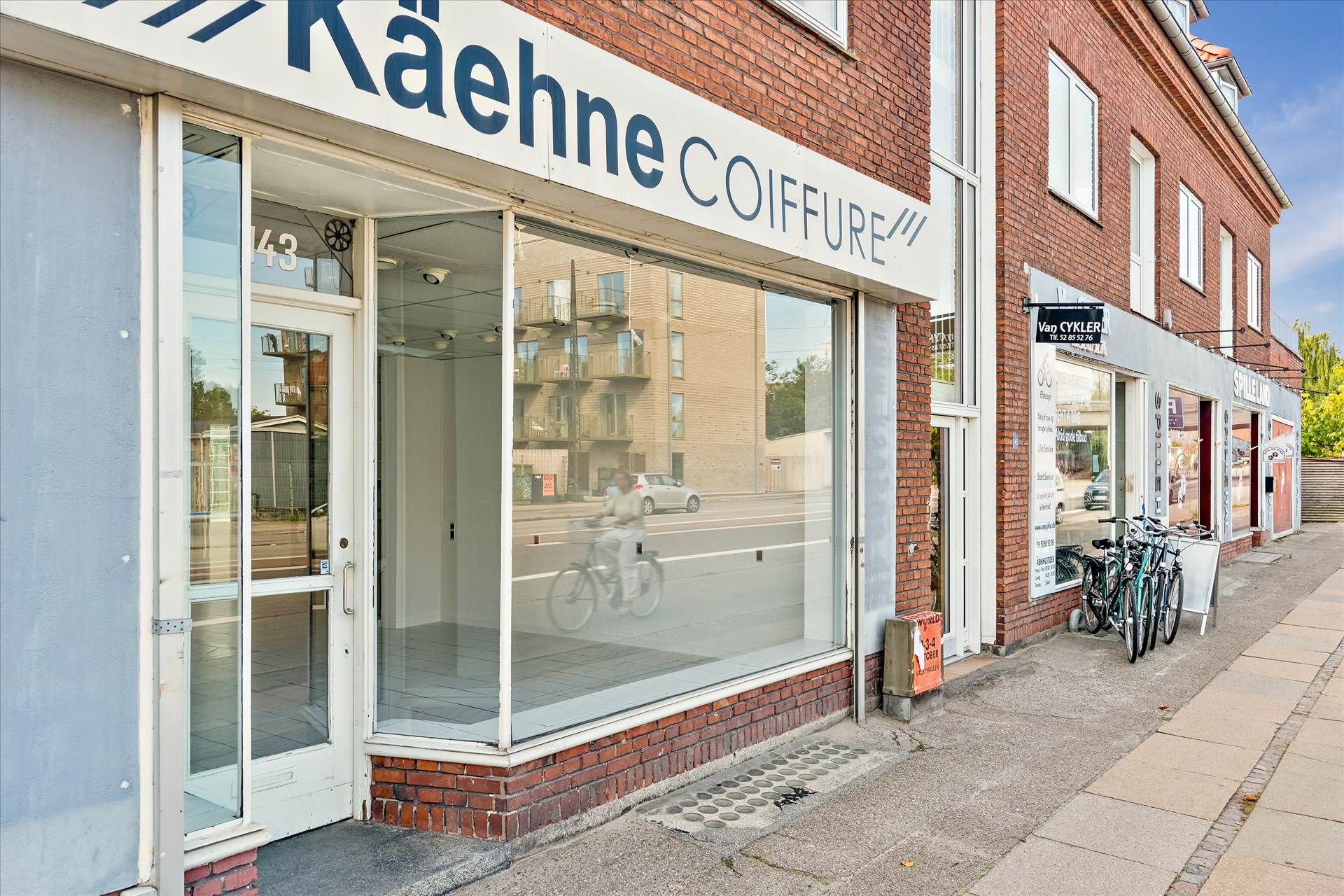 Lejemål med butik i stueplan med vinduer og dør, og cykler udenfor på gågaden
