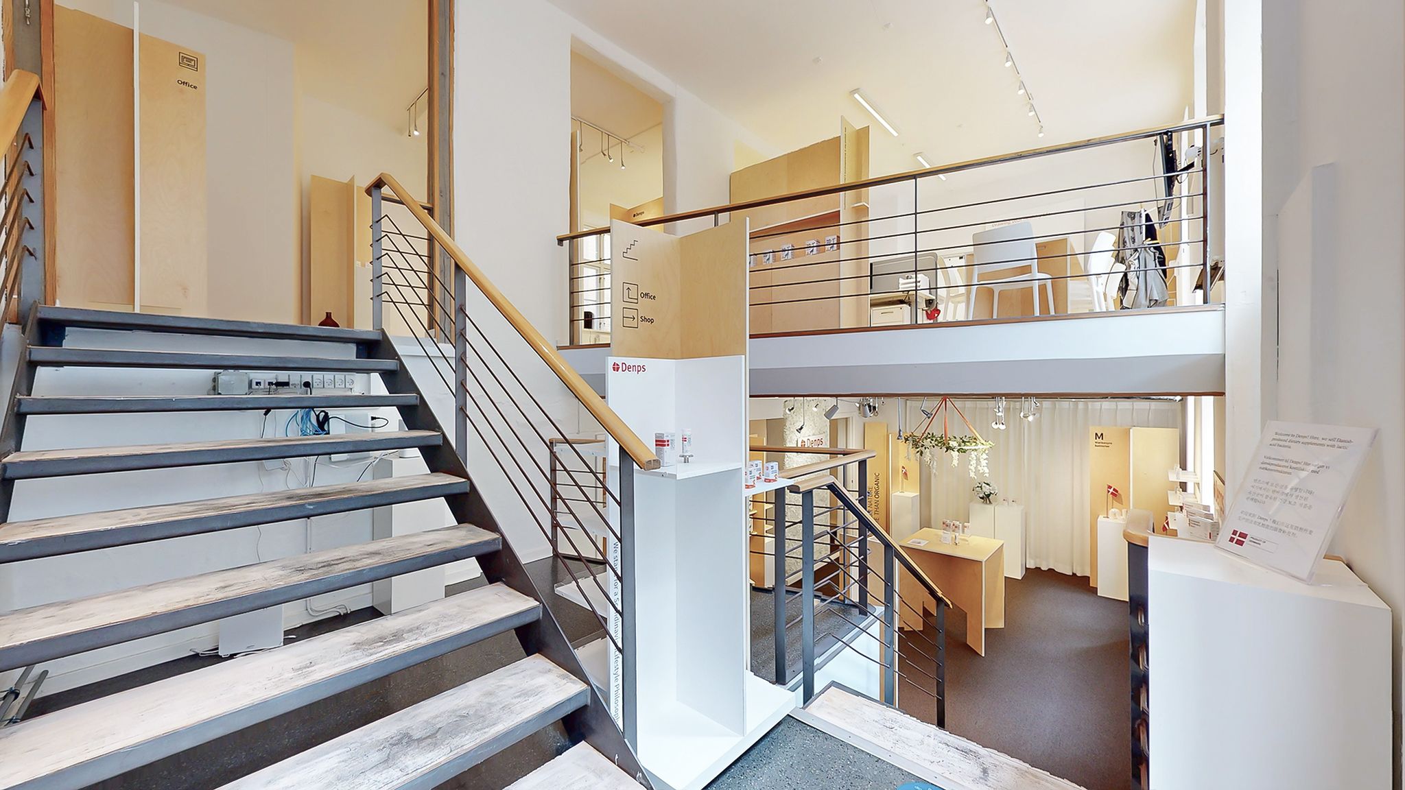 Moderne og funktionel forretningslokal med to etager, trapper og møbler, der giver et åbent og indbydende udseende