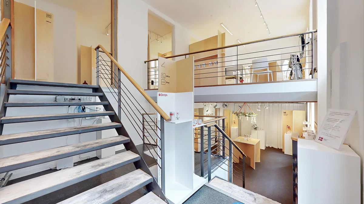 Moderne og funktionel forretningslokal med to etager, trapper og møbler, der giver et åbent og indbydende udseende