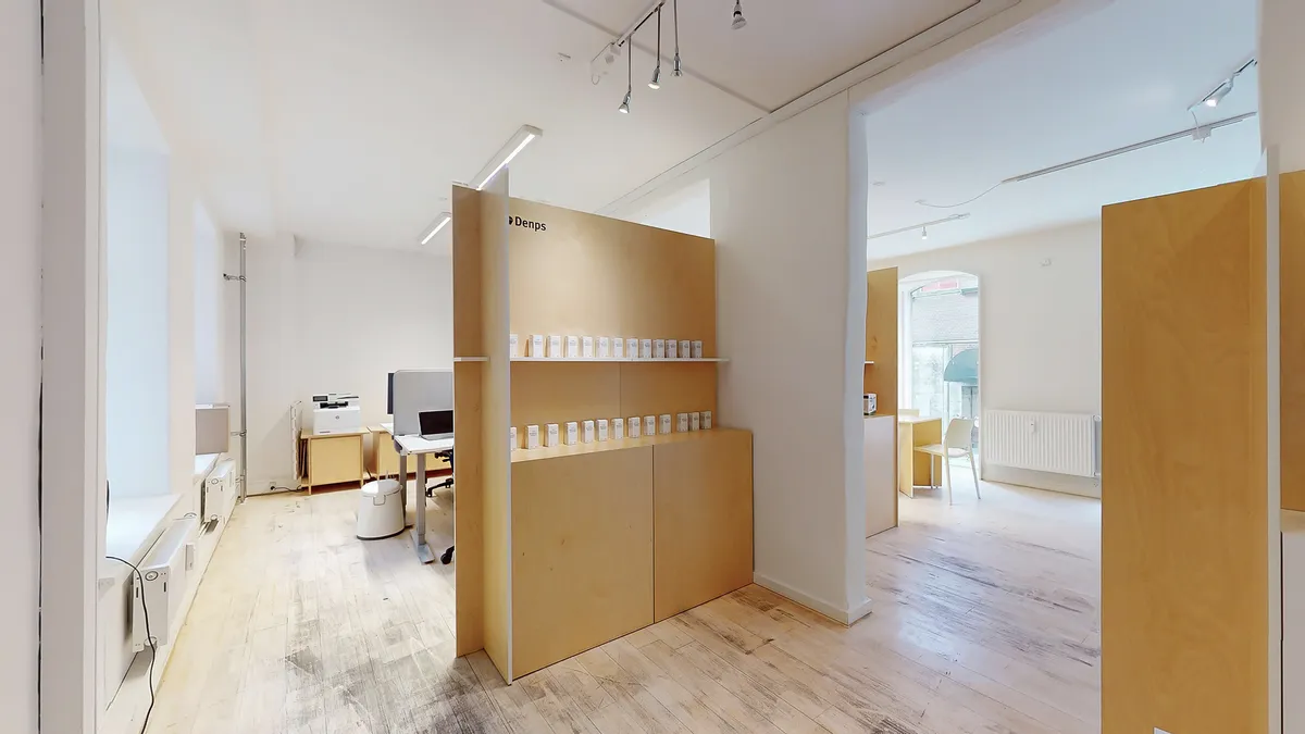 Det er et minimalistisk kontorlokal med lyse brædder og lysegule gulvbelægning. Der er en hvid hylde med små kasserede