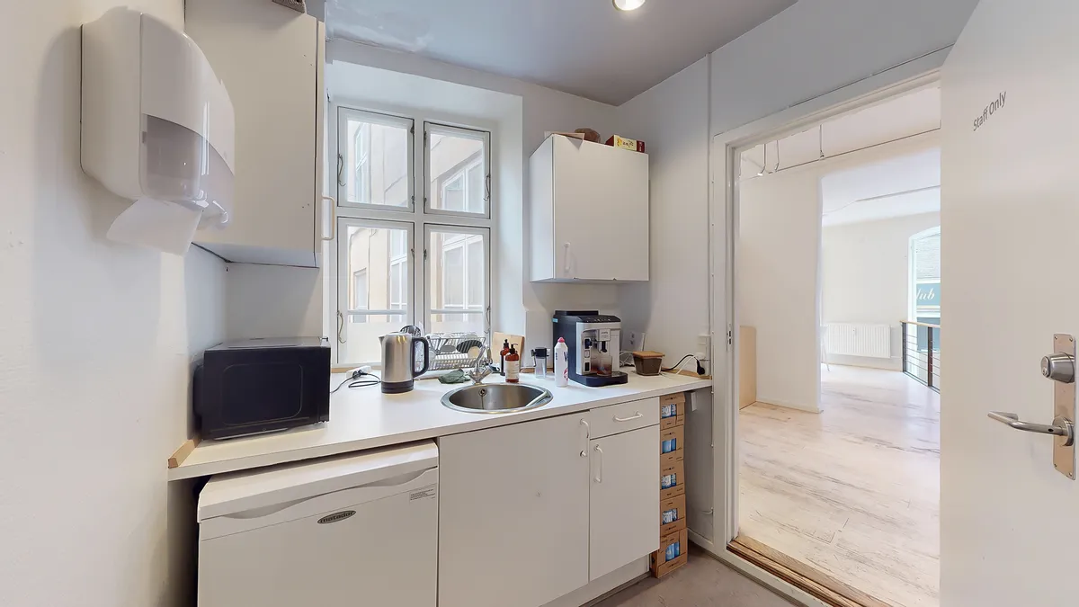 Moderne køkken med hvide skabe og diske, en mikrobølgeovn, kaffemaskine og køleskab med flere kassevarer. Køkkenet har hvide