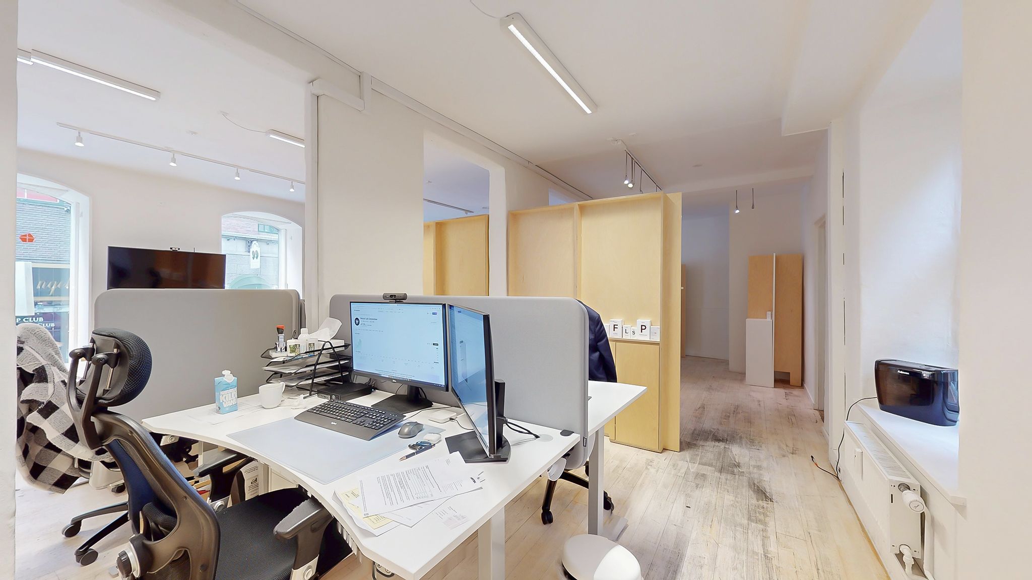 Et moderne kontor med to skriveborde med computere og to sædestole. Skrivebordene er placeret ved siden af hinanden og har