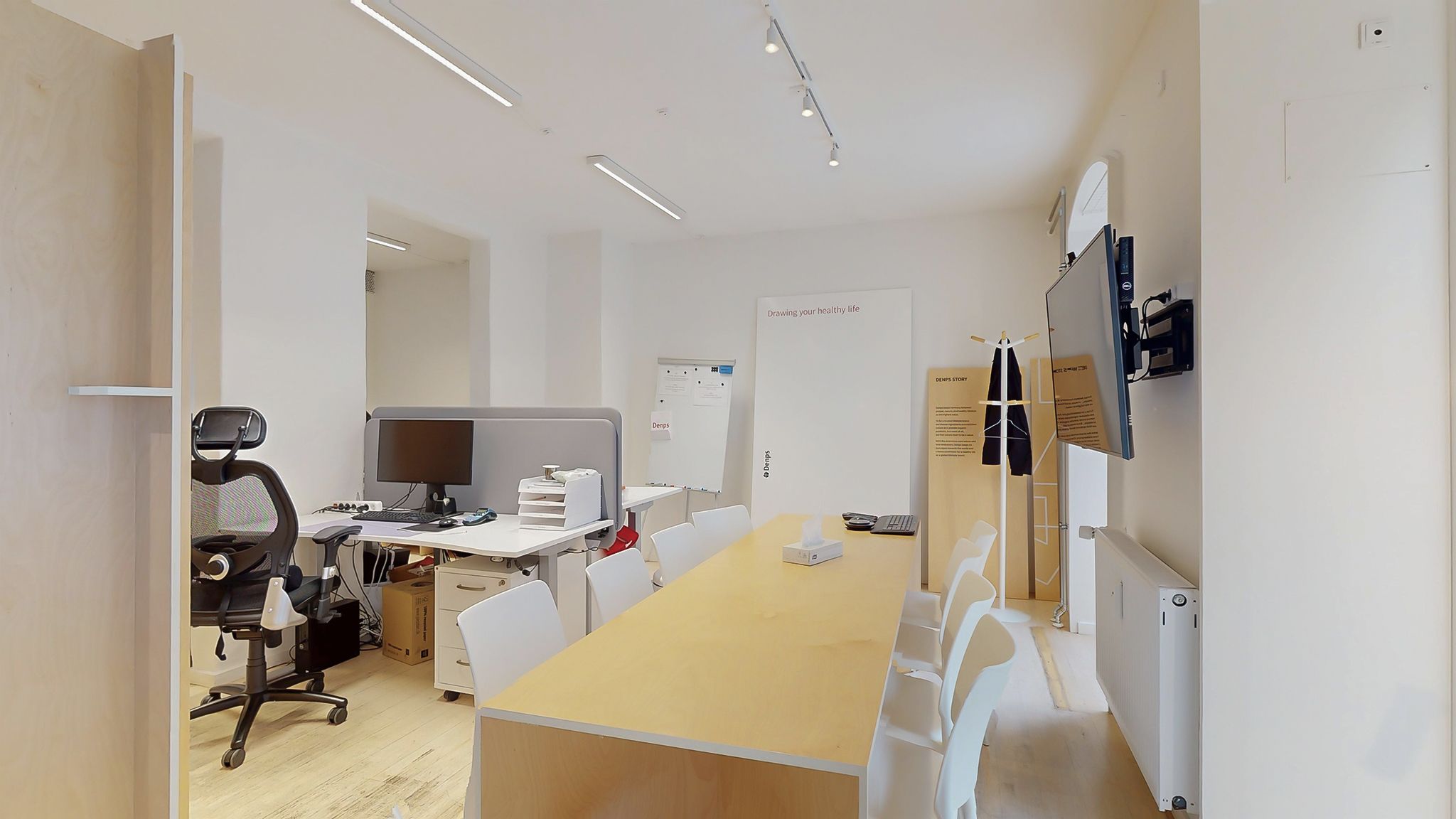 Moderne kontor med lyse træborde og hvide kontormøbler samt en stor tv-skærm og en hvid tavle med tekst