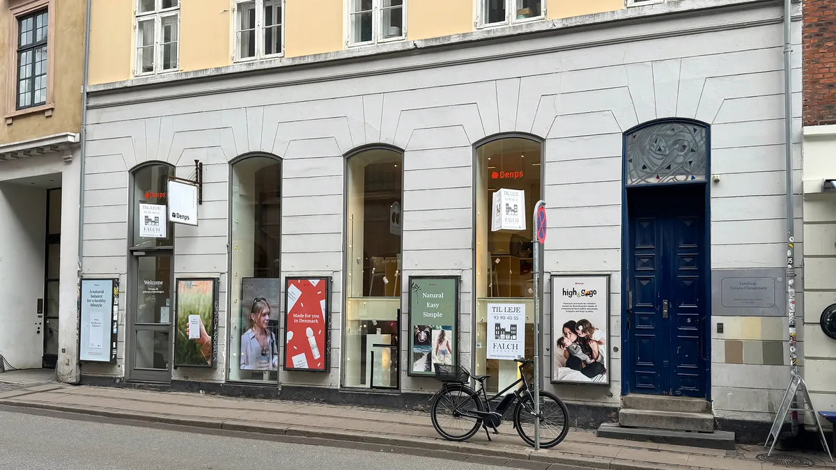 Detaljeret udsigt på det gamle hus med store vinduer, reklameskilte og cykel ved siden af facaden. Den blå dør og