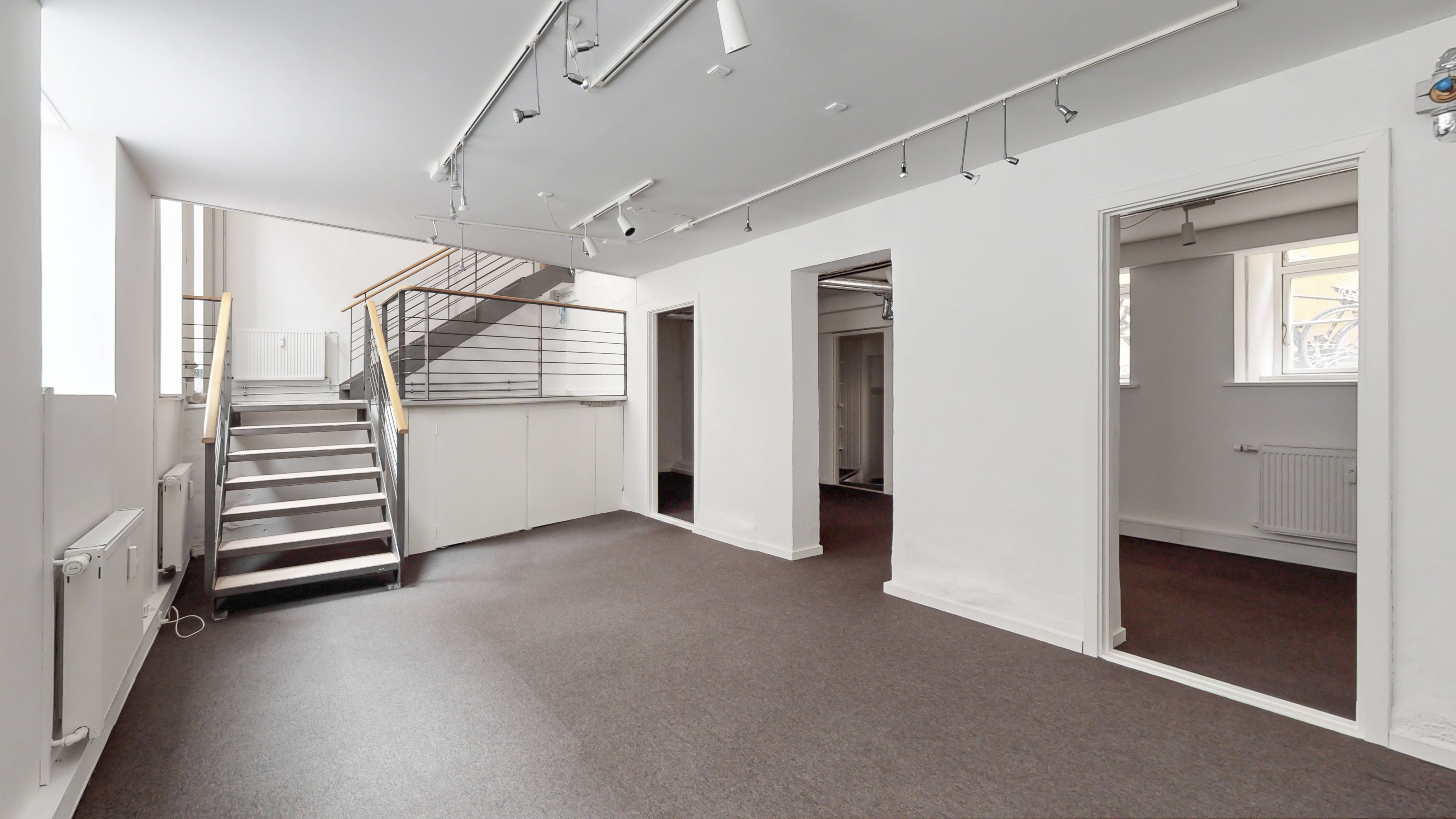 Lys og ren indretning med hvide vægge og gulv samt stige til første sal. Moderne lysekroner og radiatorer samt åbne døre til siderum