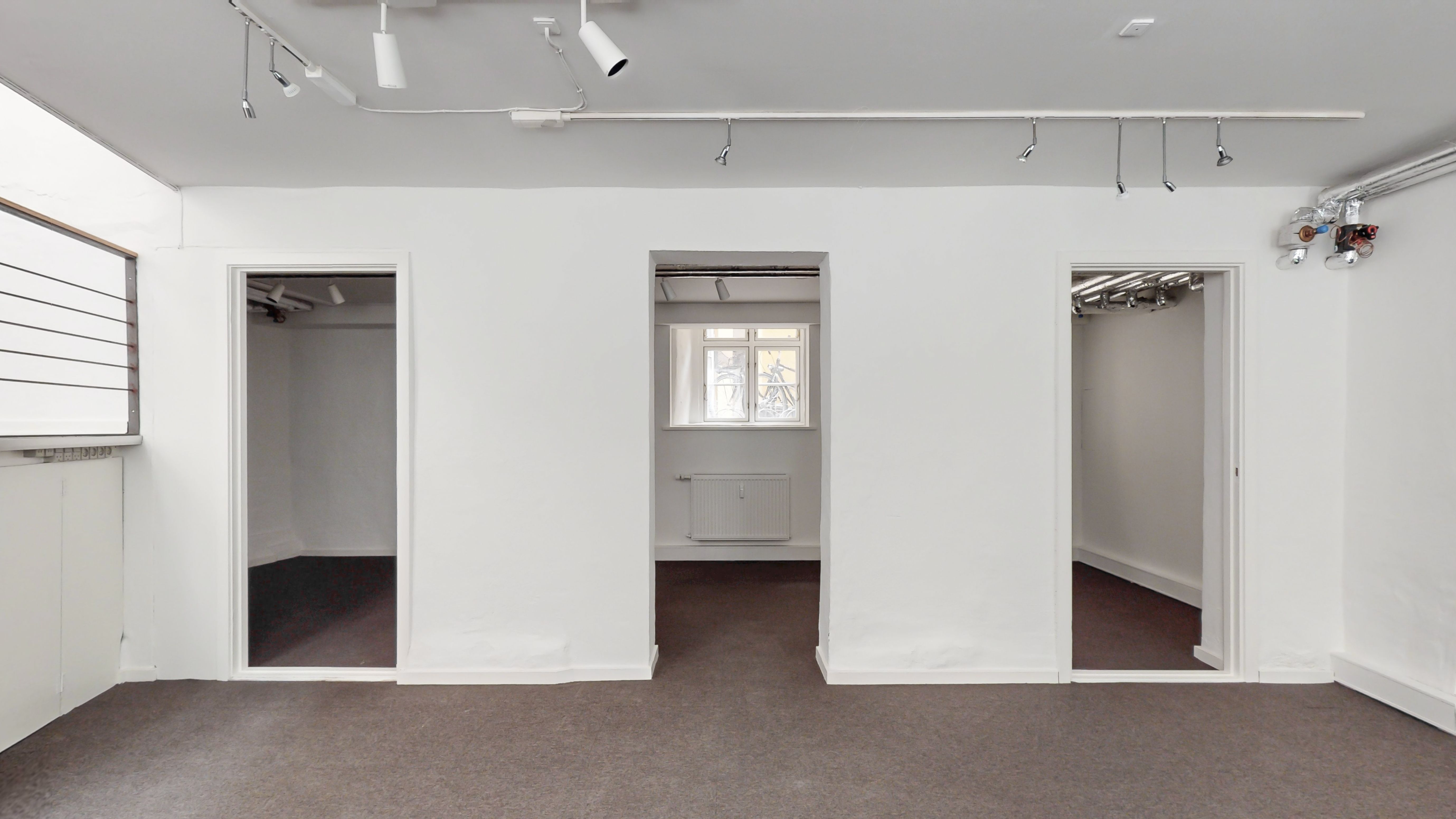 Store, tomme lokaler med hvide vægge, gulvbelægning og tre døre, hvoraf den midterste har et vindue med udsigt til gaden med cykler