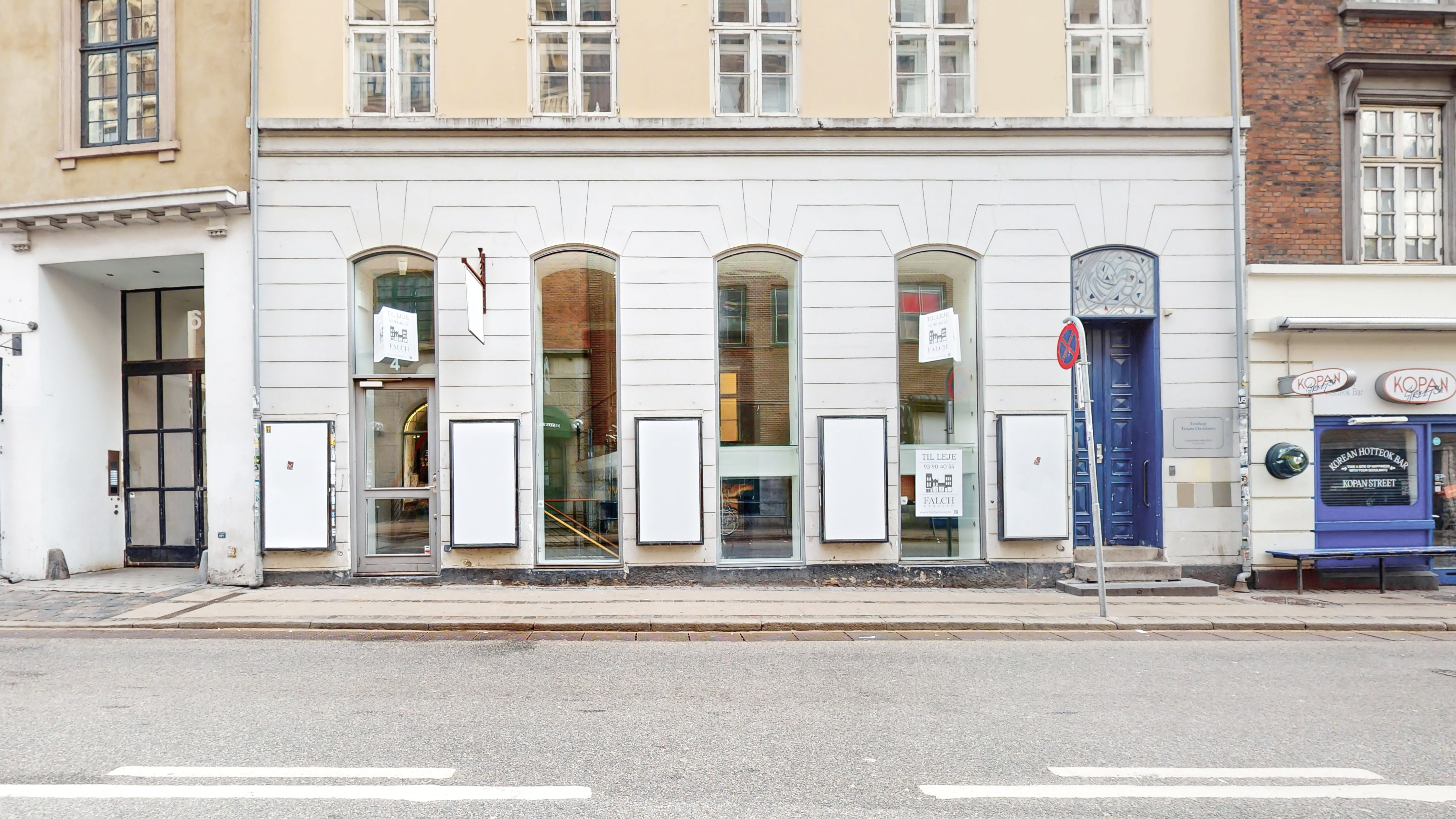 Butikslokale i hjertet af Indre By med tomme vinduer og hvide døre, der er lukket og reklameannoncer i glasvinduet