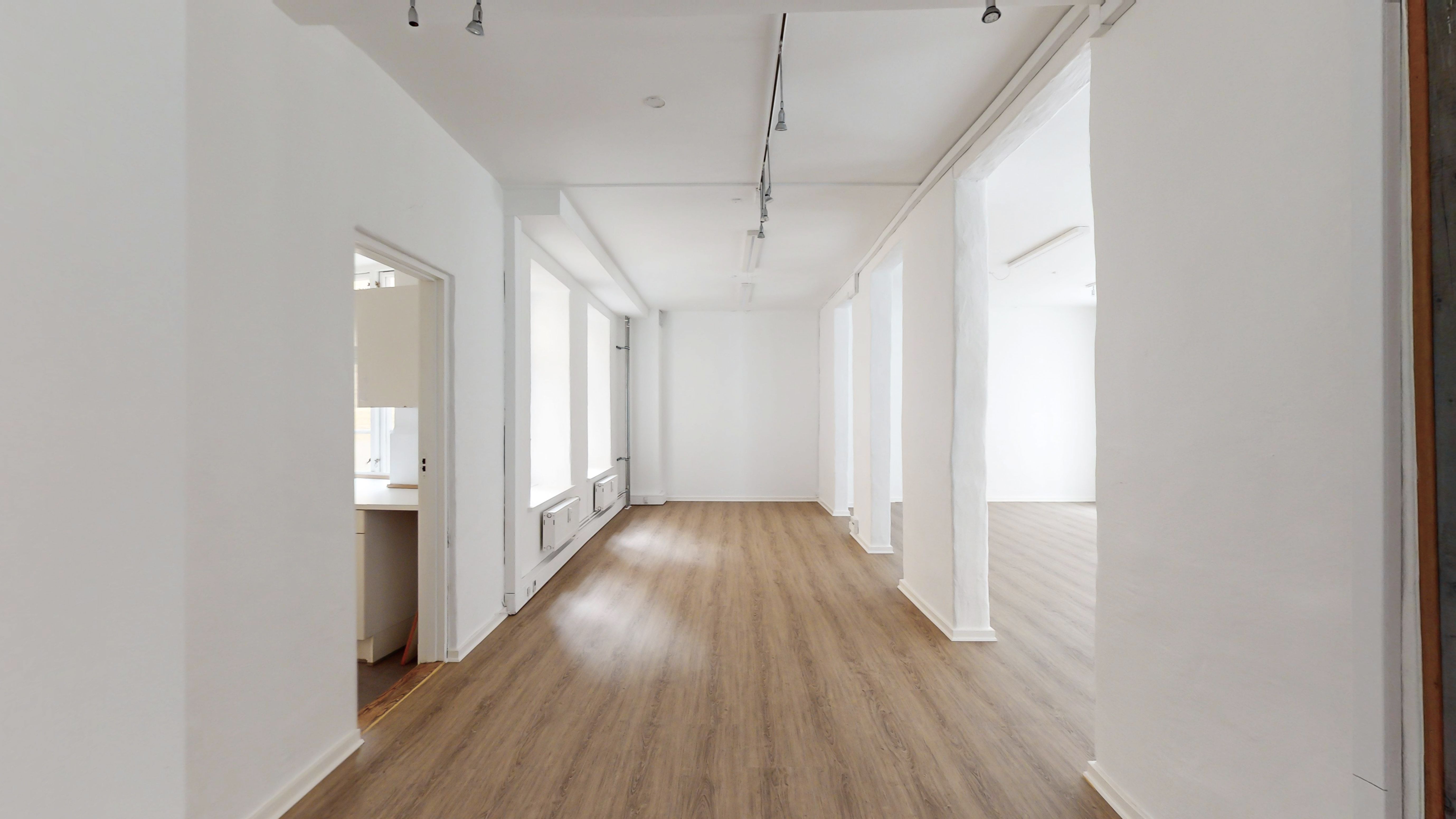 Hallen med hvide vægge og lyse gulvbelægning er velkomstværdig. Loftet er hvidt og udstyret med hængende lysekroner. To lyse døre fører ind i siderum.