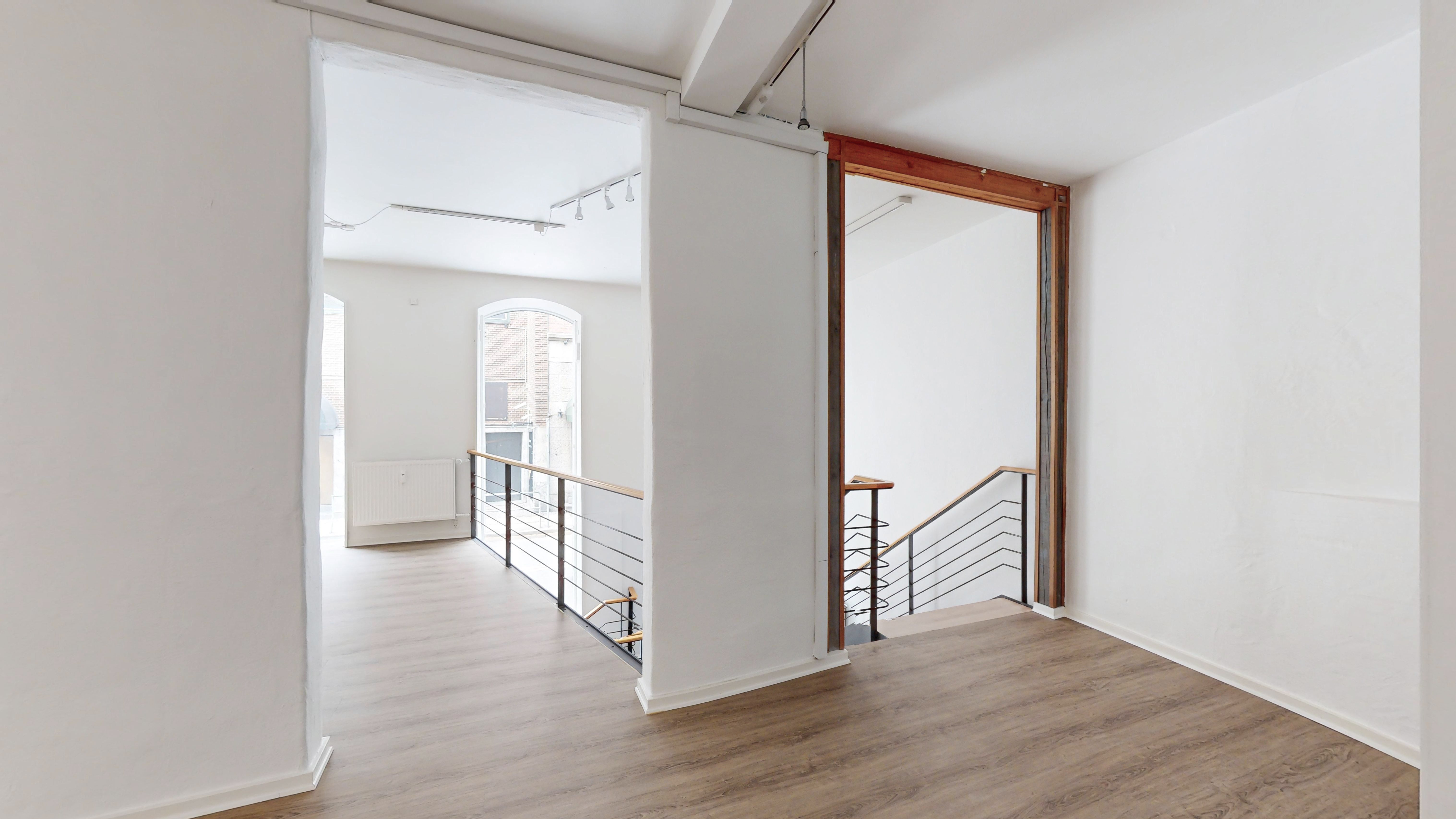 En stor og lyse stue med trægulv og hvidt gulv, hvor der er et skrapeled og en stige til øverste etage. Der er lysekroner i loftet og et højt vindue på en side.