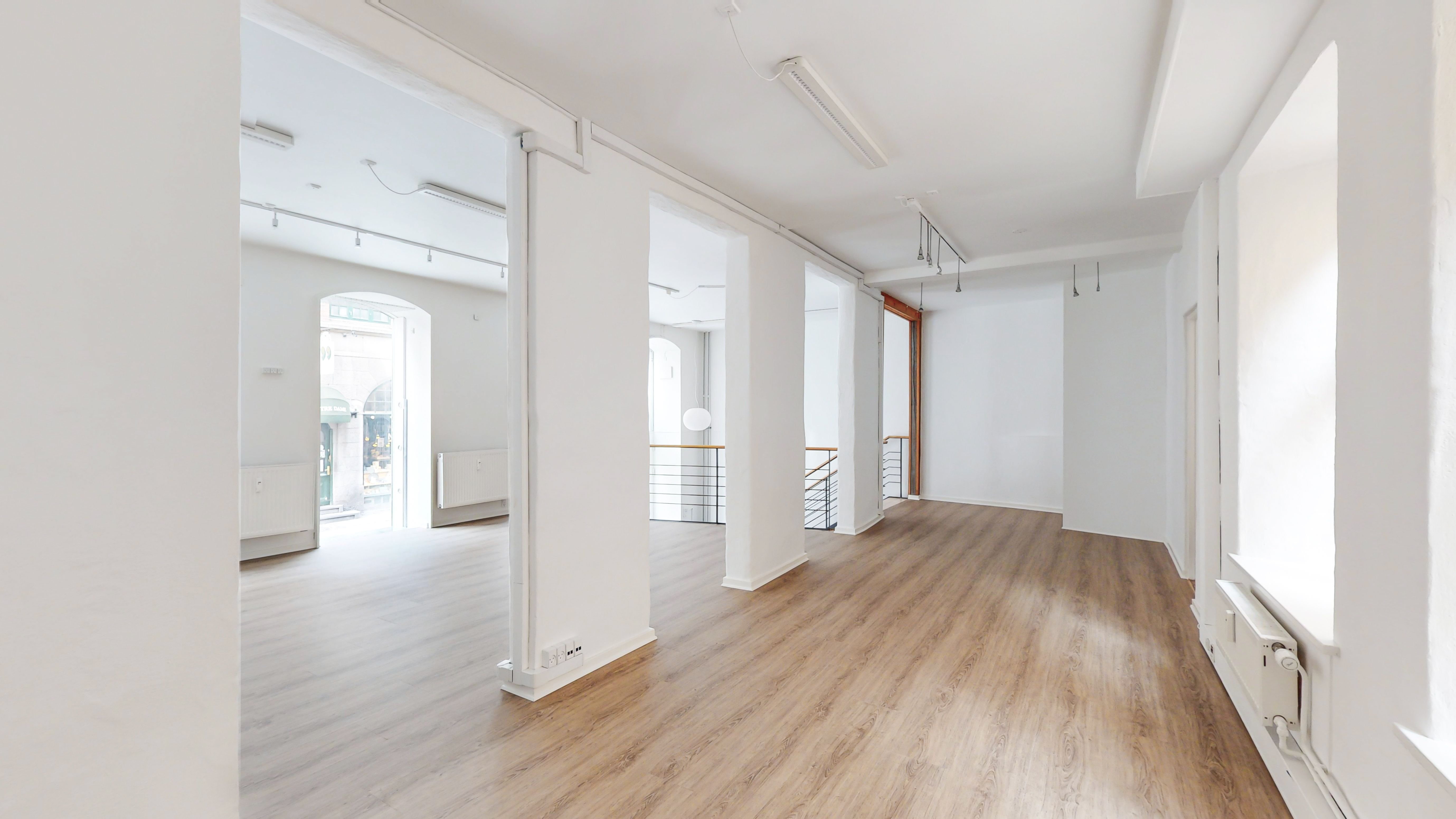 En stor, tømret, hvidmalet butikslokale med lyse, trægulve, moderne belysning og åbne vinduer i hjertet af København.