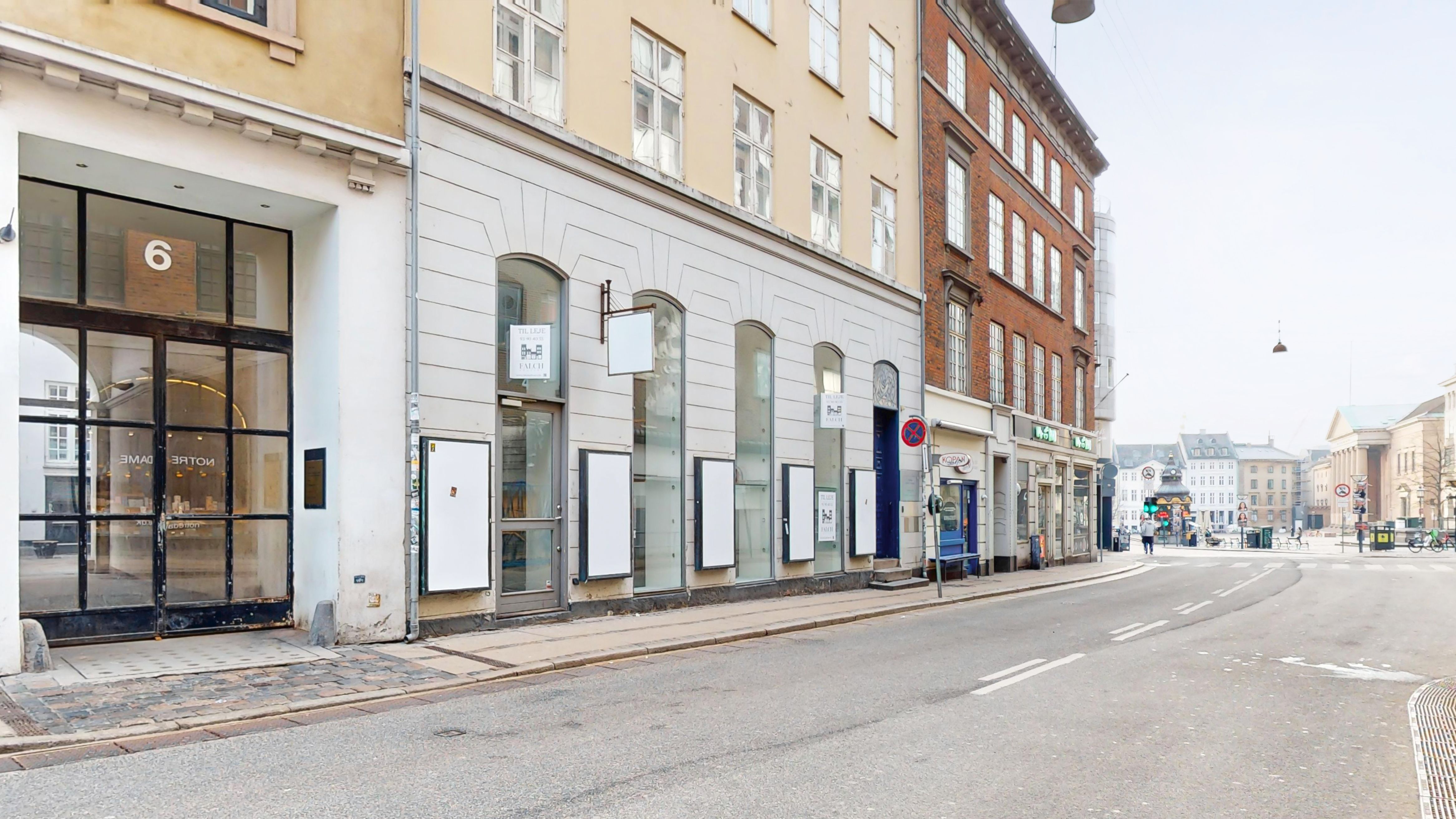 Indre By, København K, butikslokale med store glasruder og nummer 6. Værelserne er hvide med høje lofter, og der er flere butikker og gågade i baggrunden