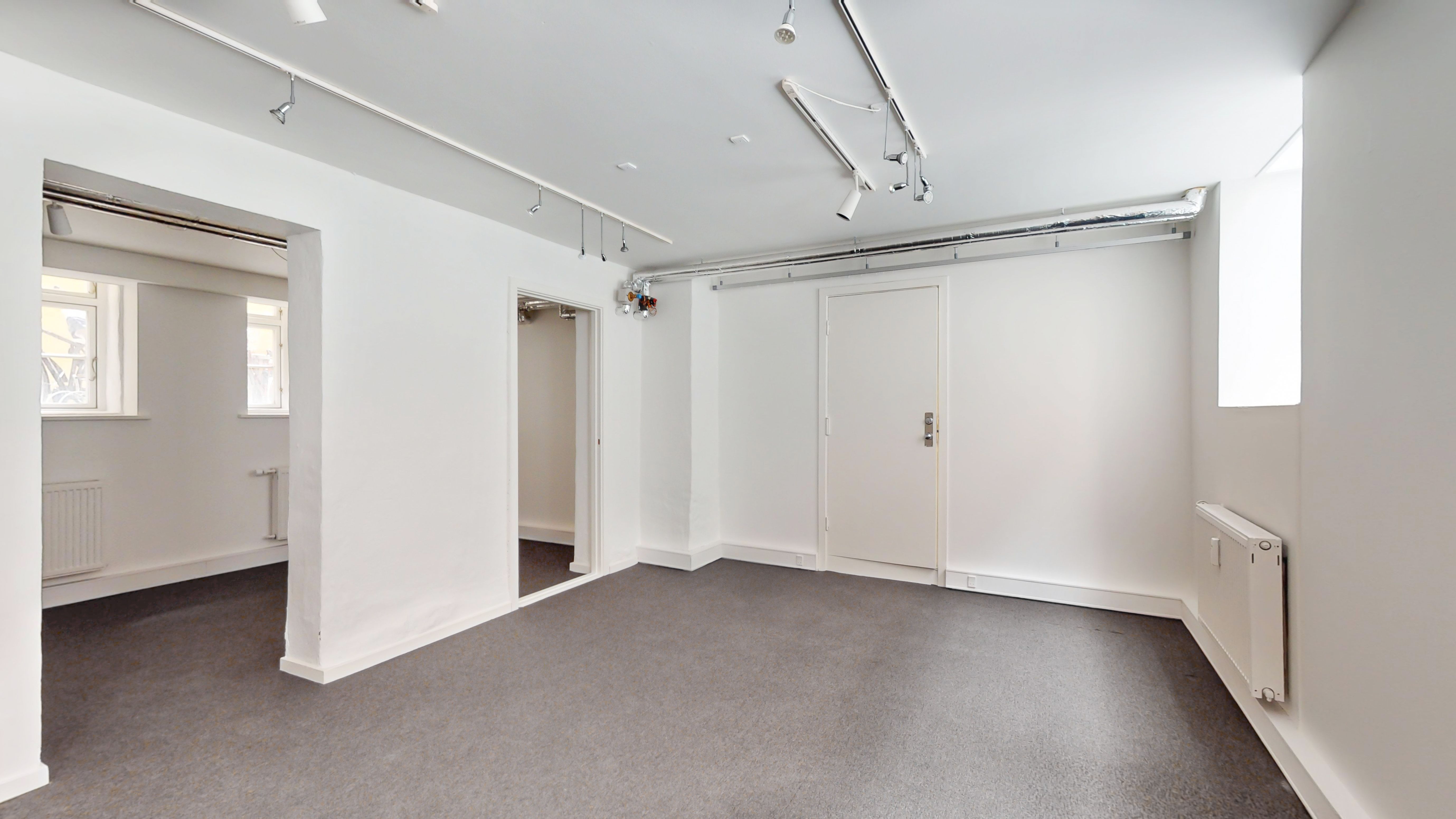 Store hvide lokaler med lysegulv og hvide vægge. Værelserne er tomme og indeholder hvide døre, radiatorer og vinduer. Loftet er hvidt og indeholder flere lyskilder.