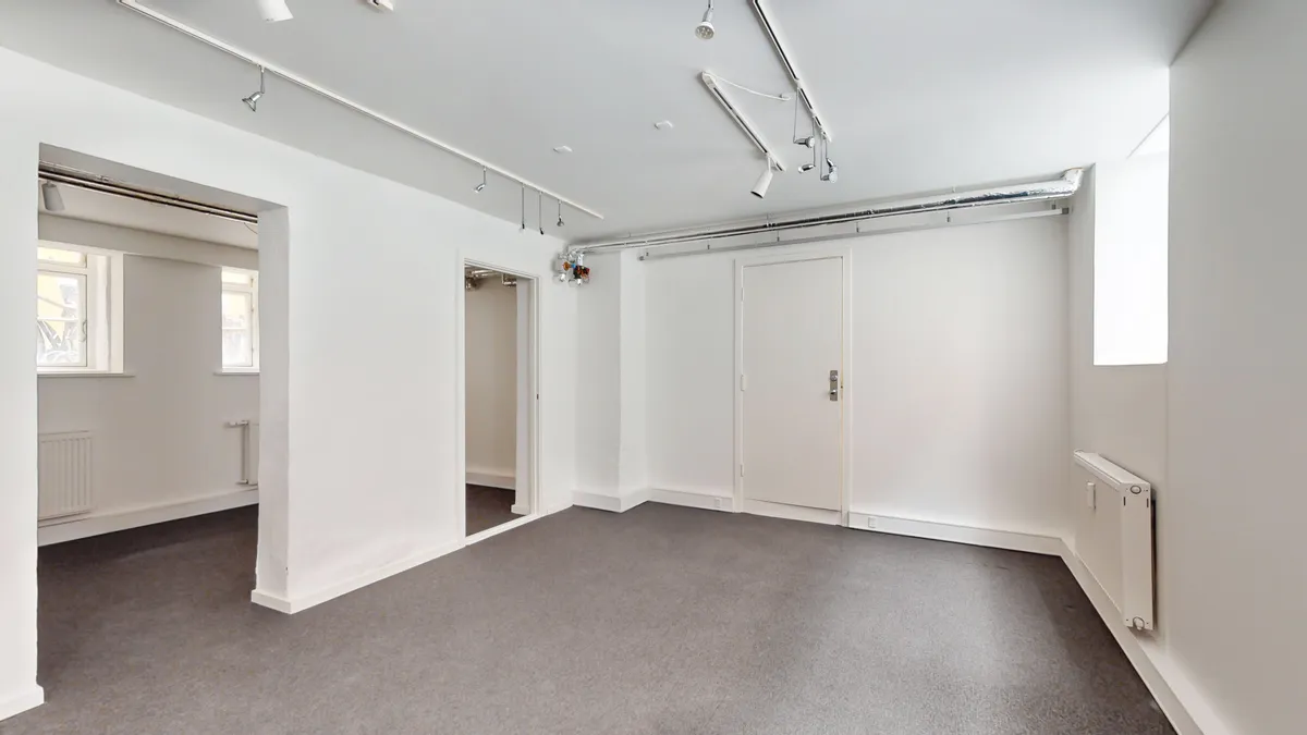 Store hvide lokaler med lysegulv og hvide vægge. Værelserne er tomme og indeholder hvide døre, radiatorer og vinduer. Loftet er hvidt og indeholder flere lyskilder.