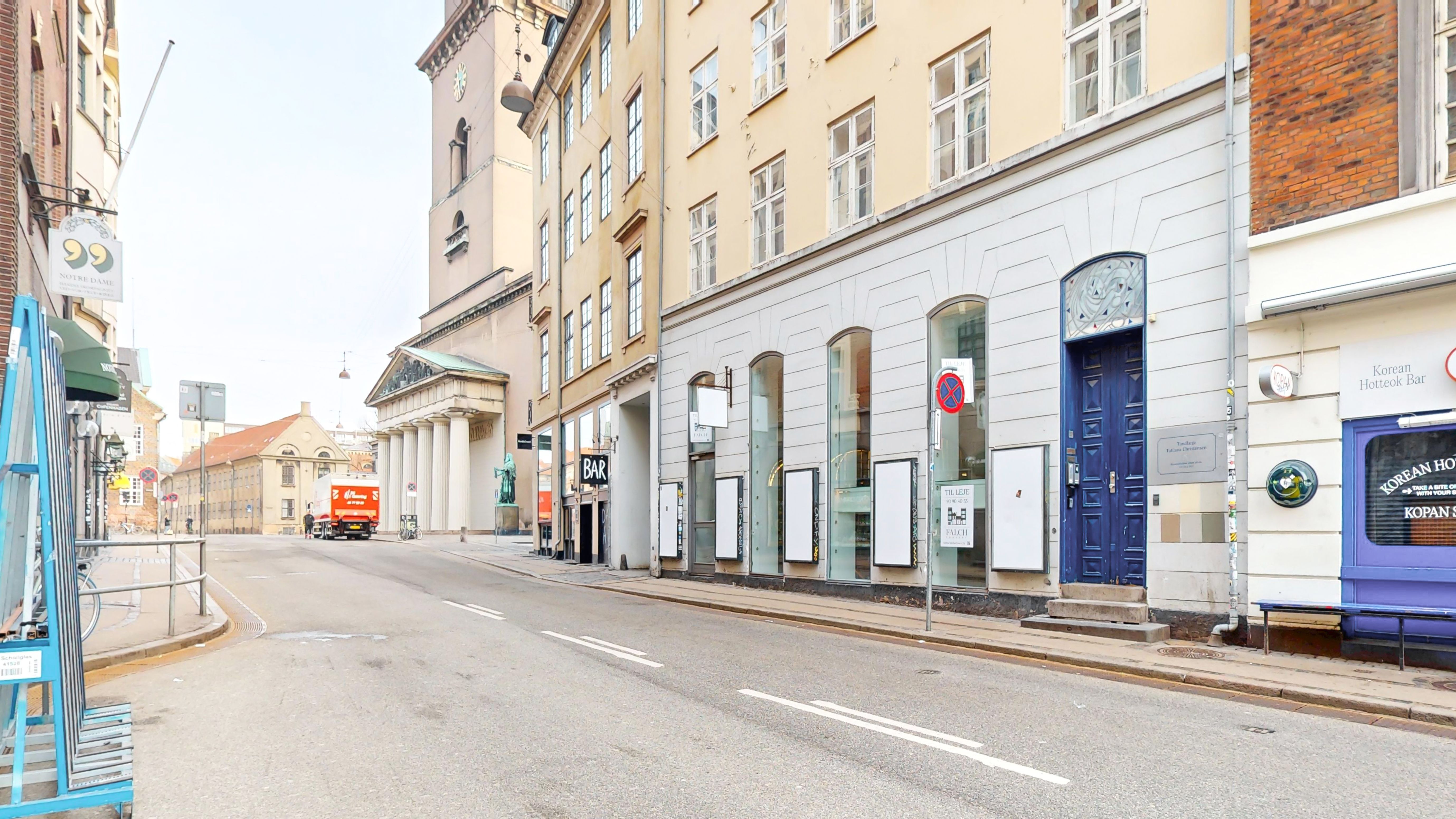 En tom gade med butikker, hvor en lastbil kører forbi. Der er et skilt med forbud for at parkere og stoppe og røde skilte med forbud for at parkere og stoppe