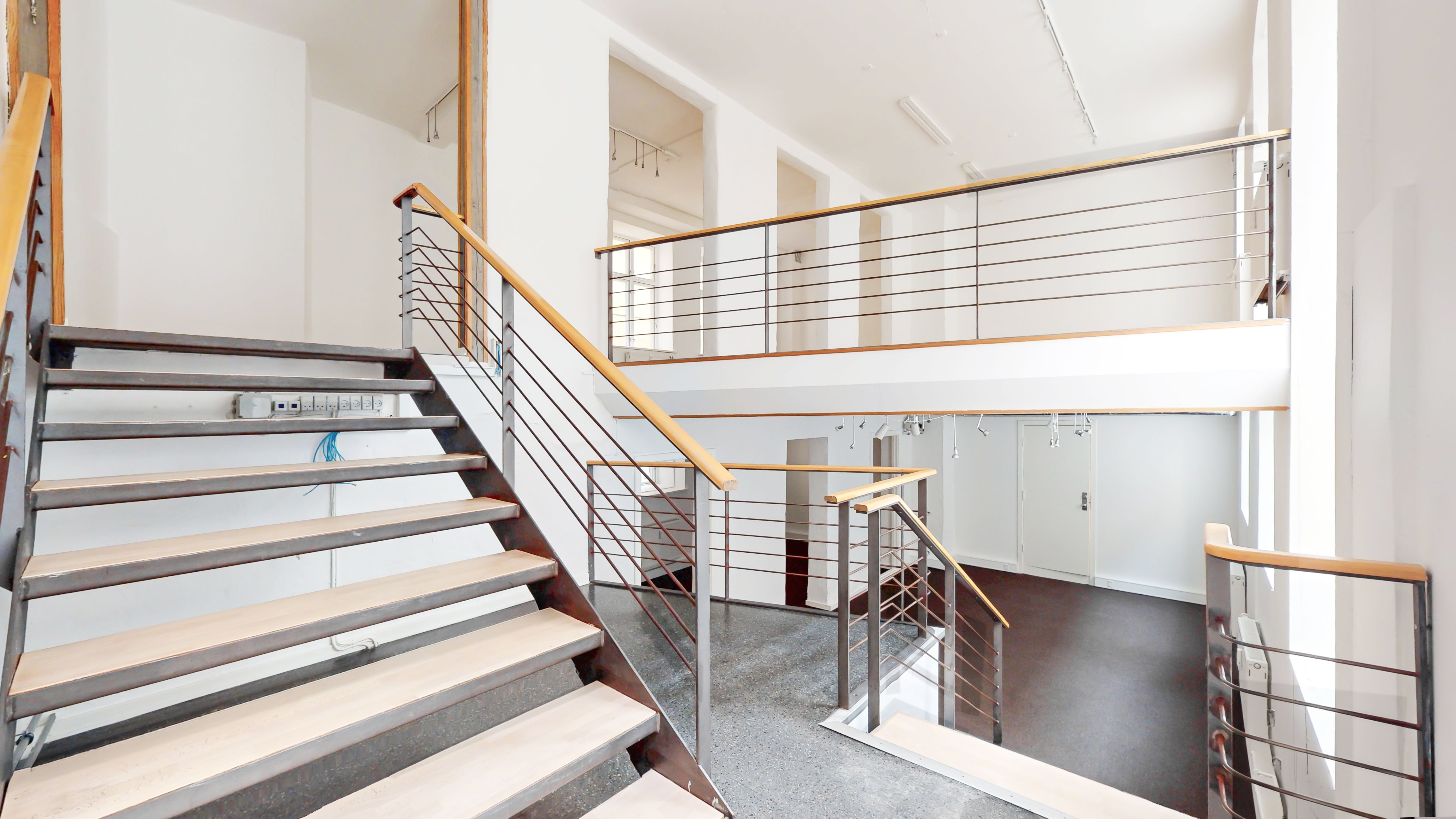 Store åbne stueplan og trapperum med lysegule trætrin og høj gulvfinish. Moderne håndtag på trapperummet og lysstofrør. Hvide vægge og lofter, store vinduer og lyse loftsrum.