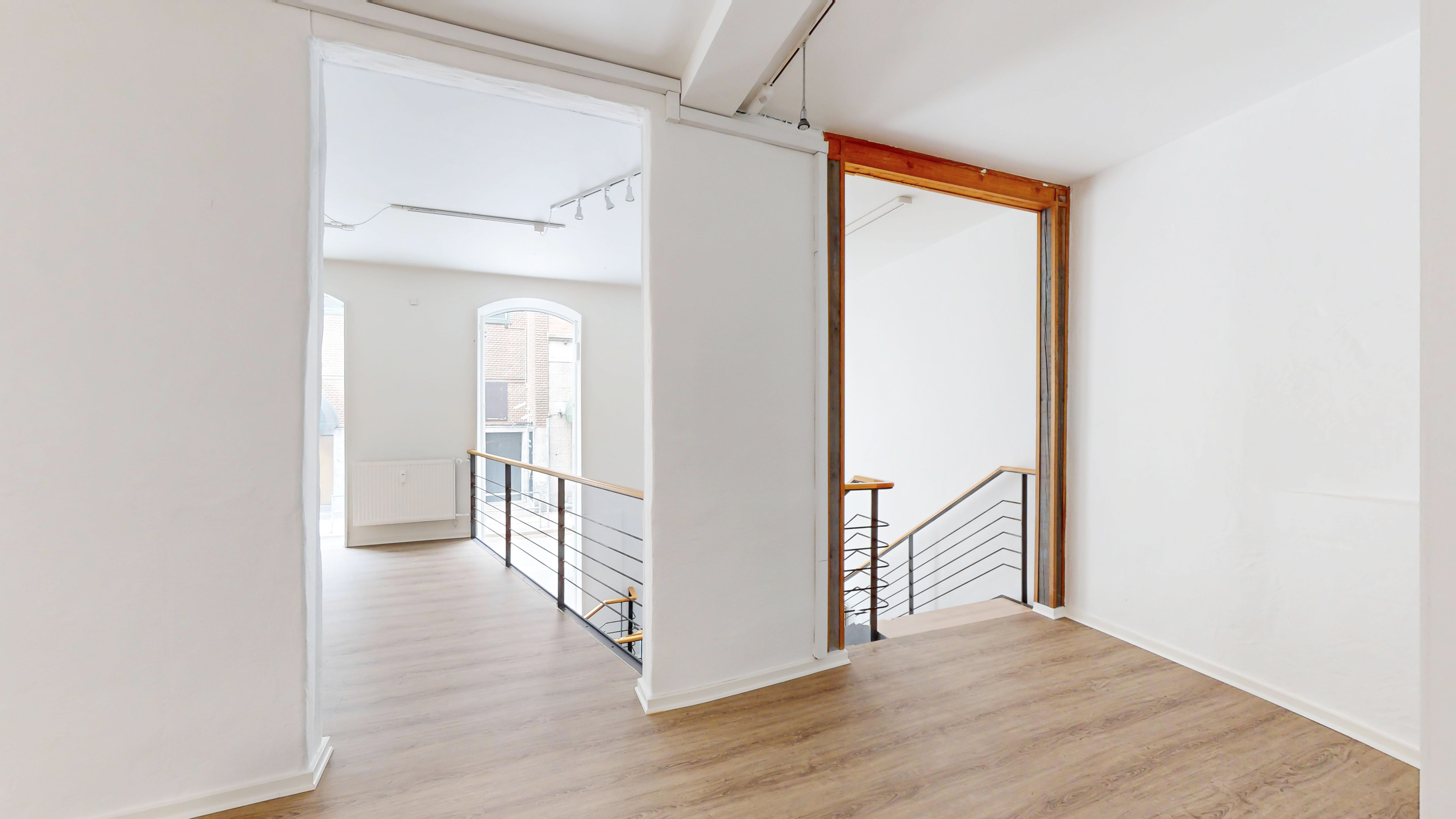 Tomten med lyse vægge og gulvtæppe. Der er en trappe med metalhåndtag og trætrin og et vindue med et udsigt. Der er en radiator monteret på væggen