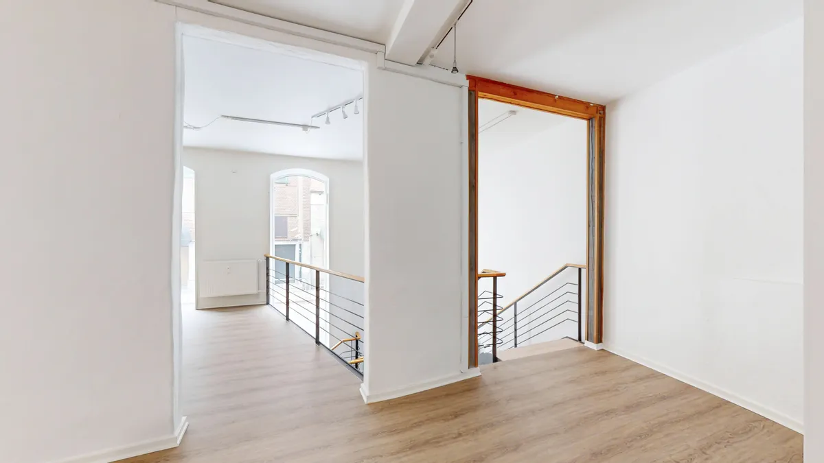 Tomten med lyse vægge og gulvtæppe. Der er en trappe med metalhåndtag og trætrin og et vindue med et udsigt. Der er en radiator monteret på væggen