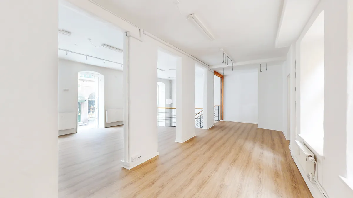 En stor butikslokale med hvide vægge og gulvtæppe og lysekroner og radiatorer på væggen