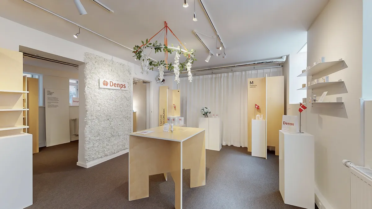 Lejemål med udsigt til gågade i København K. Et lille bord med skrift på væggen. To høje hylder med papirmærker. Flag og