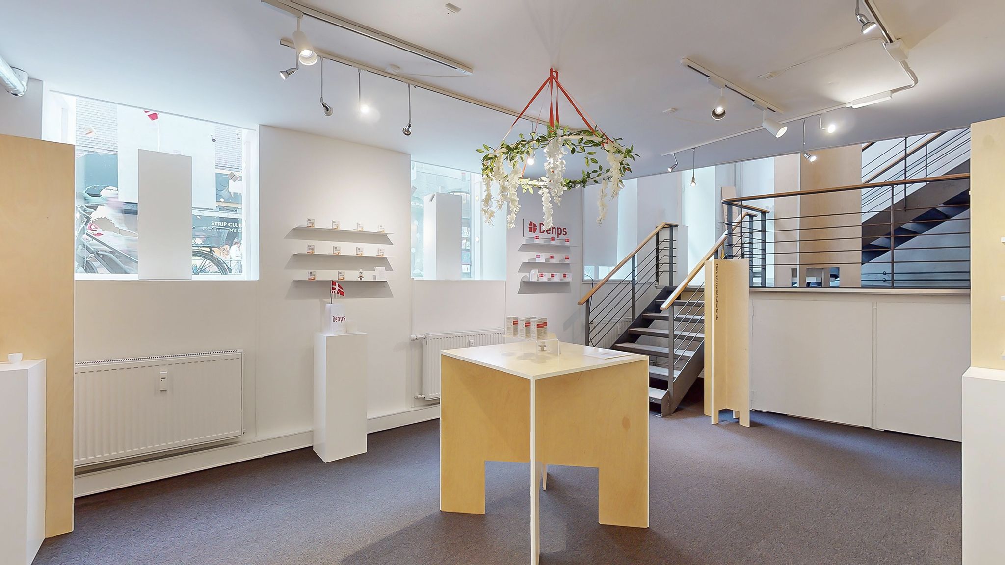 Moderne showroom med hvidt loft, hvide vægge, lysekroner og en simpel træbord med produkter