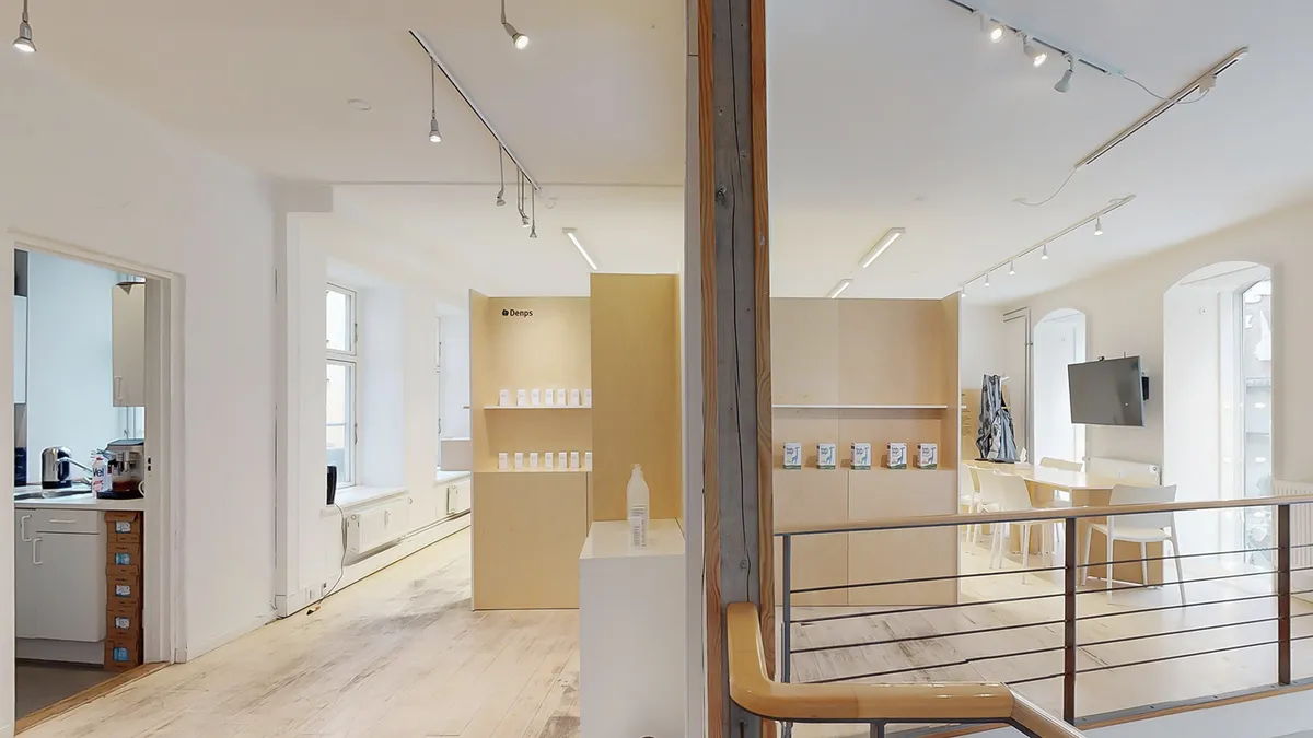 Store rum med højloft og trægulv, møbler, hylder og udstillingsborde med produkter, skrivebord og stol, vinduesbank og