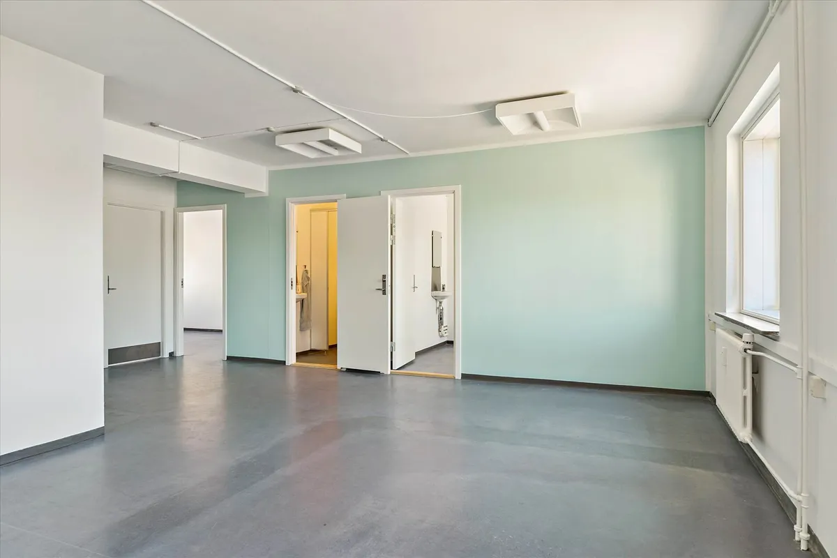 En tom, lyseblå stue med hvide vægge, lysegrå gulv og åbne døre til andre værelser og en radiator