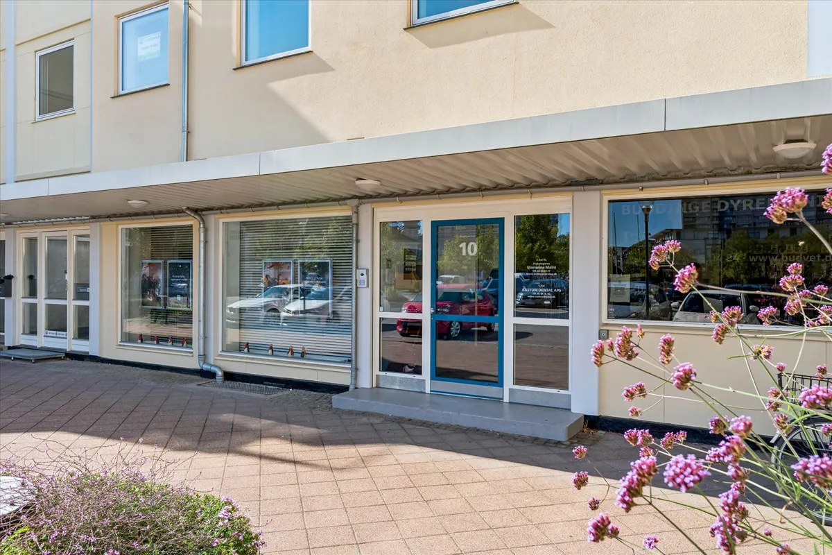 Lejlighed i Bagsværd Torv 10 med store vinduer, blå dør og blomster udenfor samt biler i spejlet