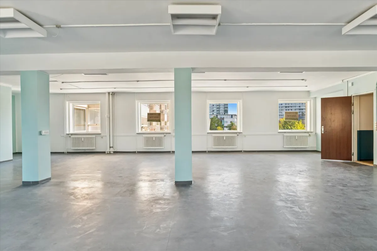 Lyse og rummelige lejemål på 247 m² med vinduer og hvide vægge samt lysegrå gulvbelægning.