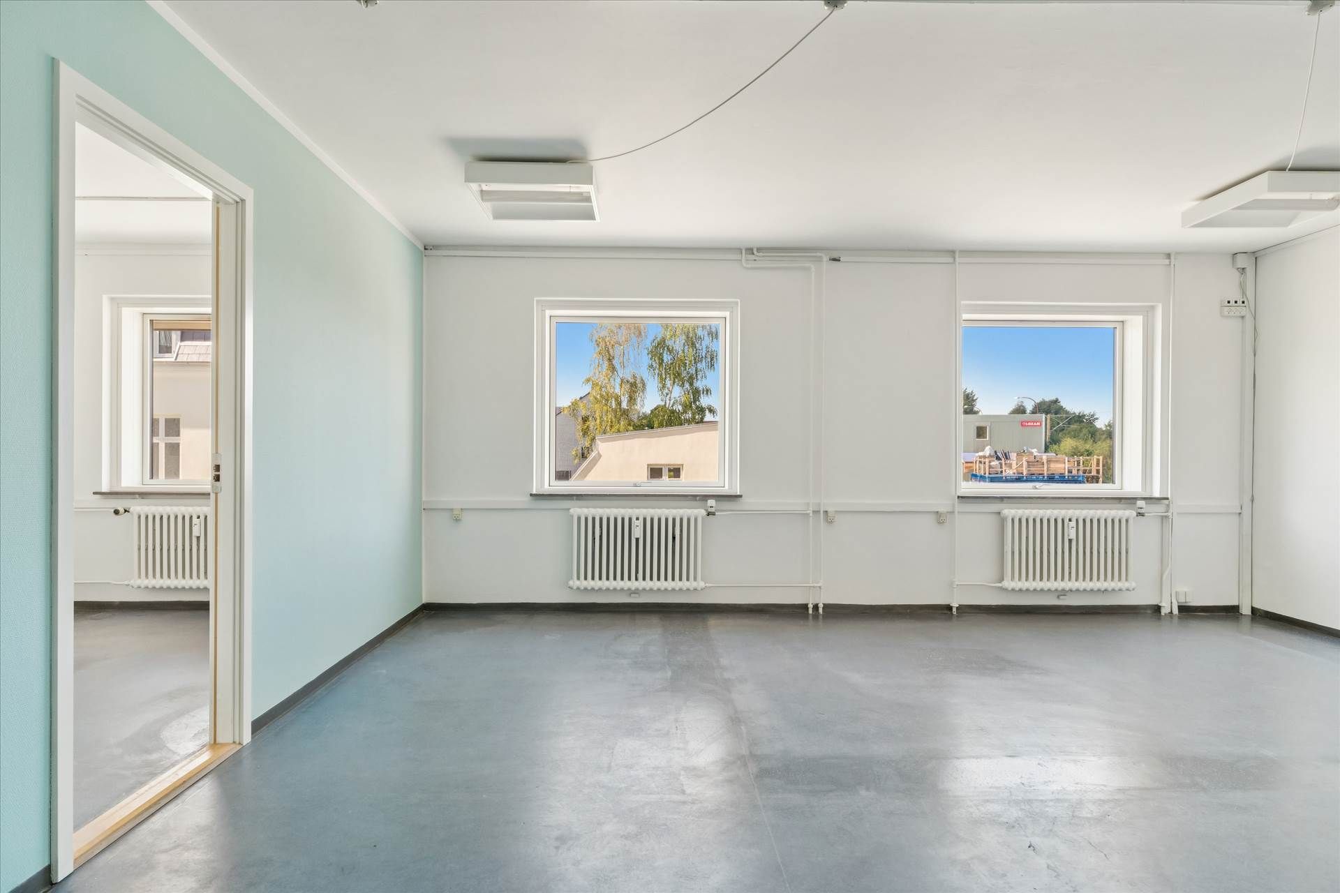 Lejlighed med to vinduer og hvide vægge og loft samt hvide radiatorer og lysegul væg på den ene side